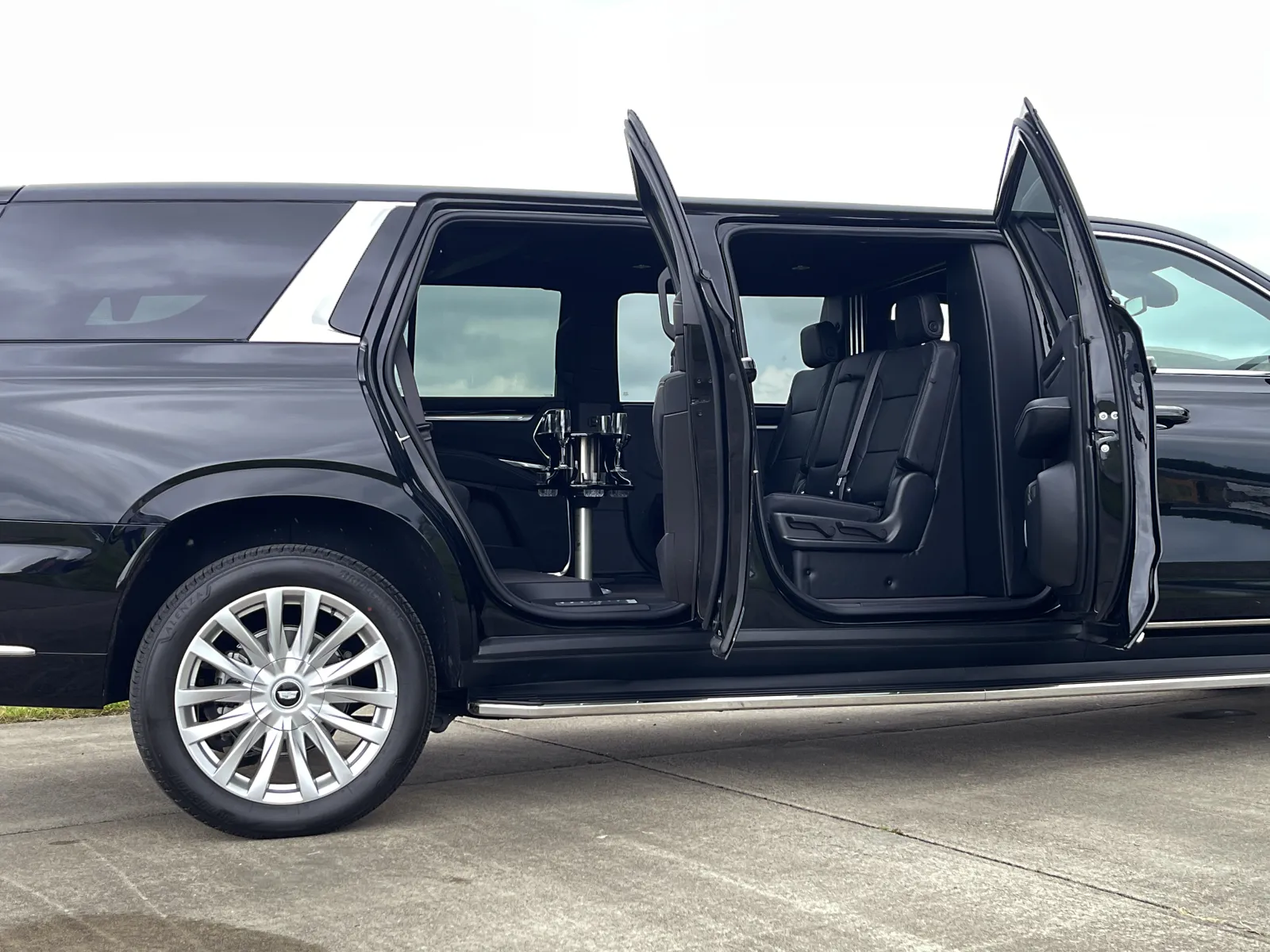 Black luxury SUV with rear doors open revealing spacious leather interior and a center table inside.