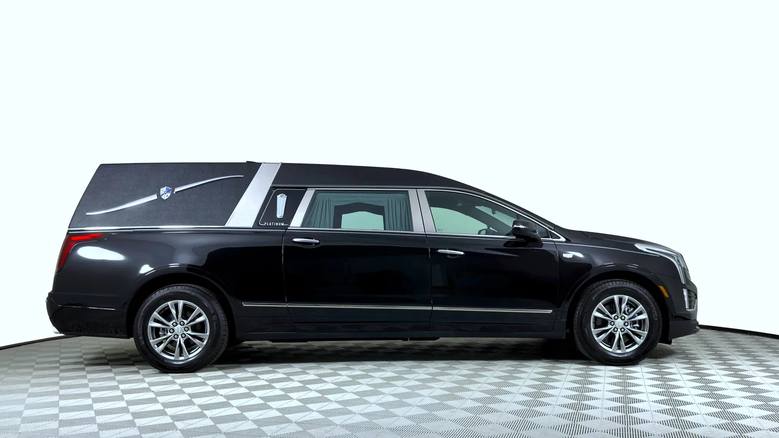 Black luxury hearse with silver accents and tinted windows on checkered showroom floor in a white studio.