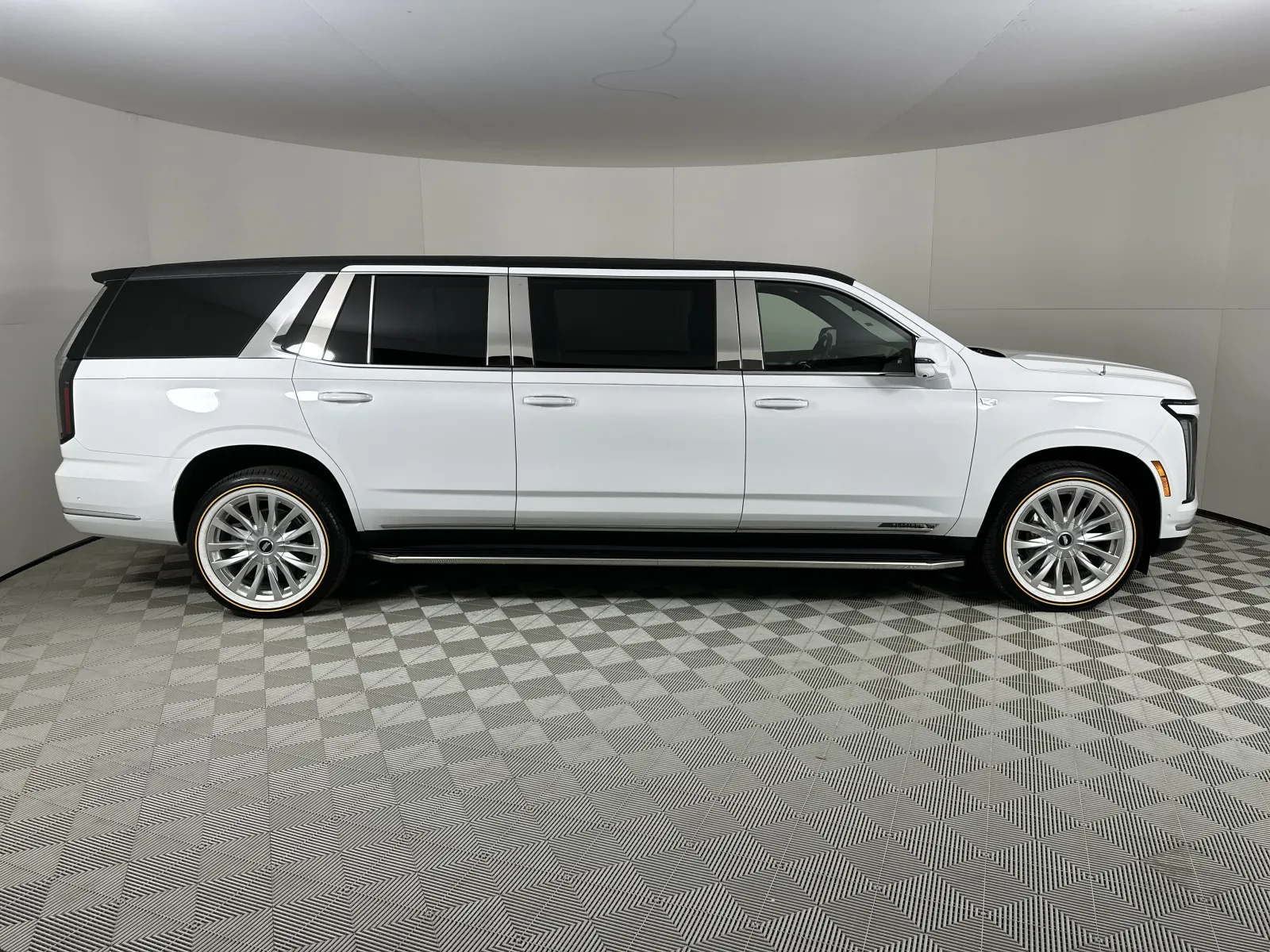 White luxury extended SUV with tinted windows and large chrome wheels in a studio setting