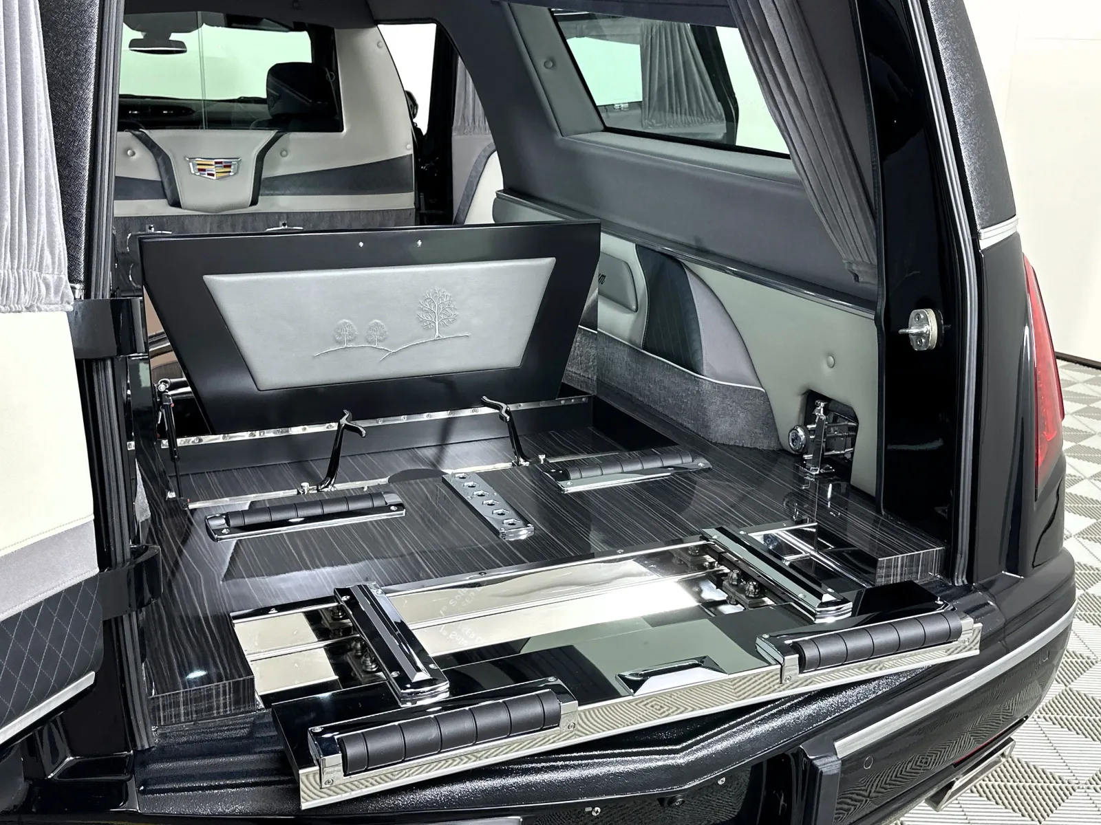 Interior view of a black hearse with polished wood and leather detailing and an open rear compartment.