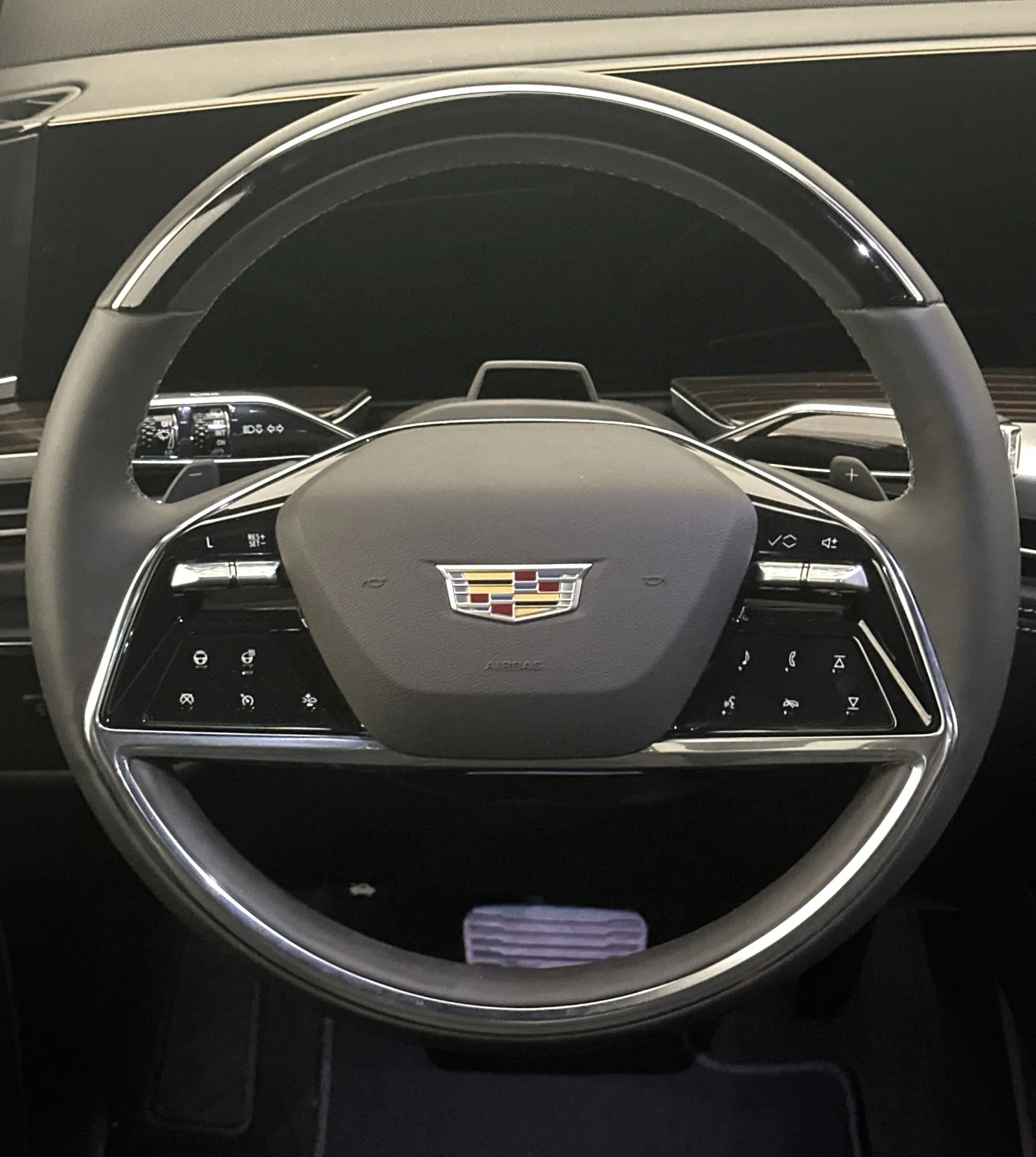 Luxury Cadillac steering wheel with control buttons and emblem inside a modern vehicle interior.