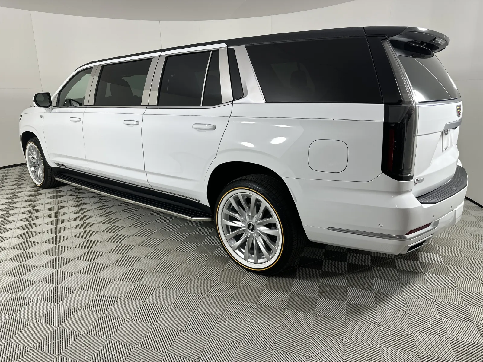 White luxury extended SUV with tinted windows and chrome rims displayed in a showroom with checkered flooring.
