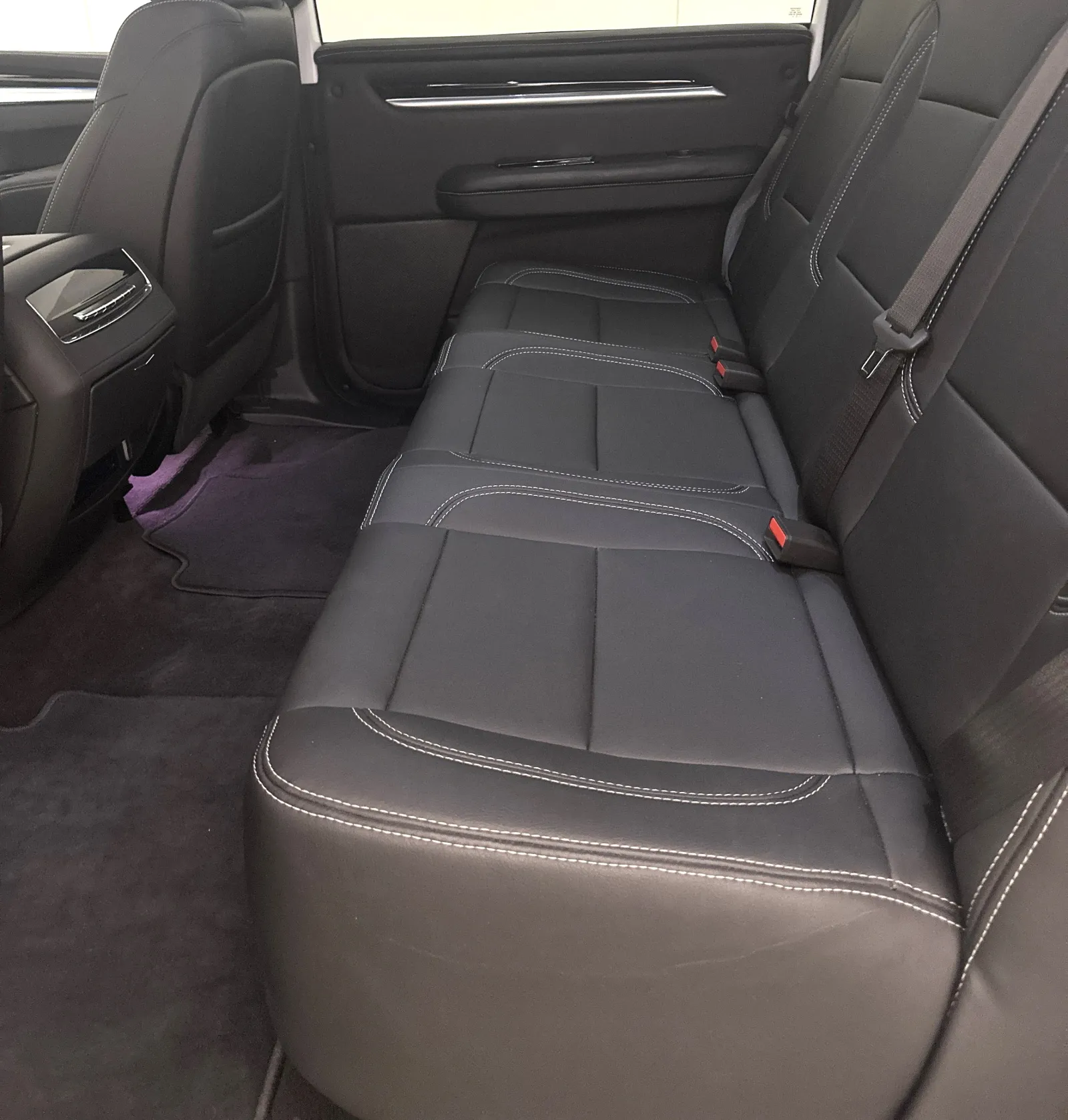 Spacious backseat interior of a car with black leather seats and white stitching