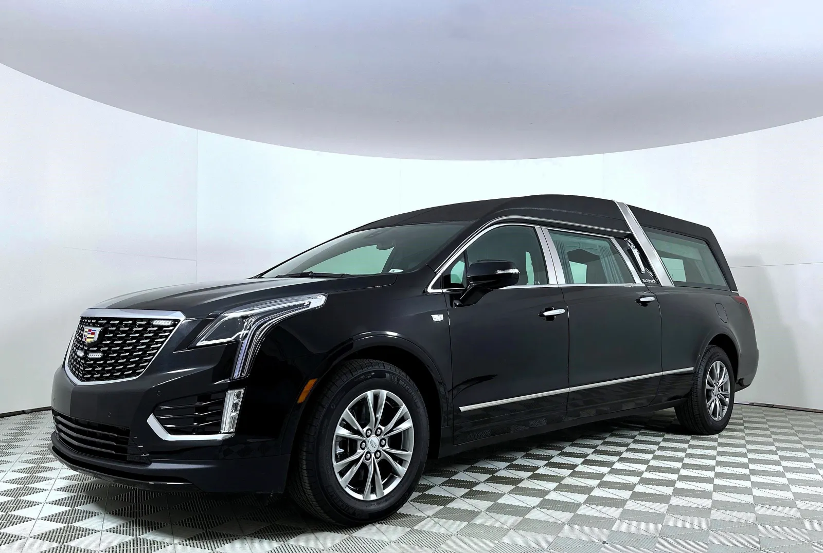Black Cadillac hearse with chrome details on a checkered floor in a white studio setting.