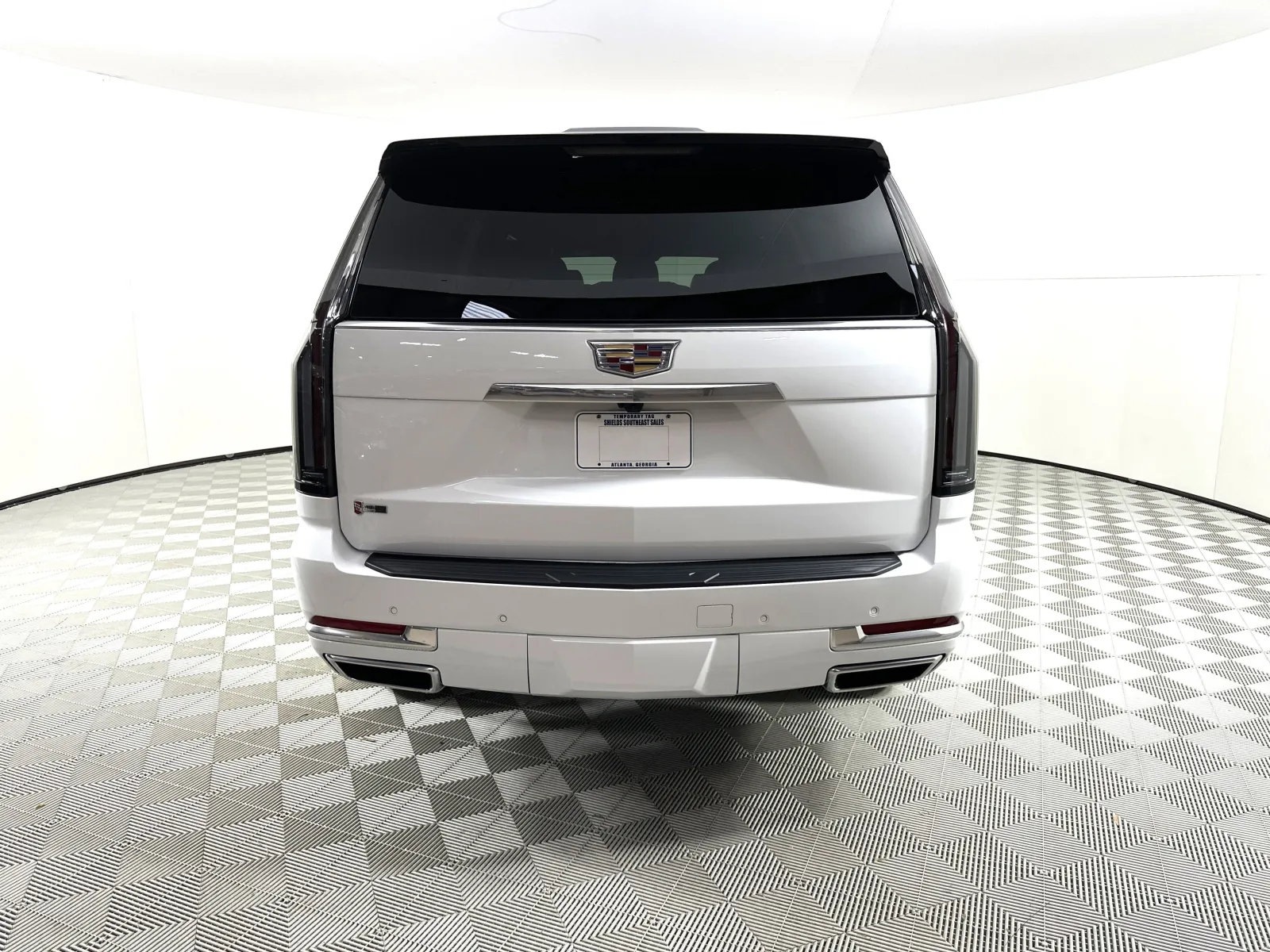 Rear view of a white Cadillac SUV in a well-lit showroom with checkered flooring and tinted windows.