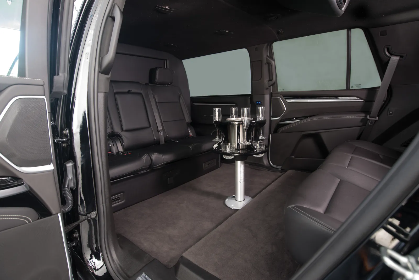 Luxury vehicle interior with black leather seats and a central table holding glasses and a bottle.