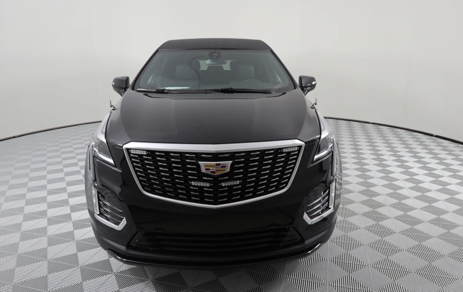 Front view of a sleek black Cadillac XT5 SUV on a checkered floor background.