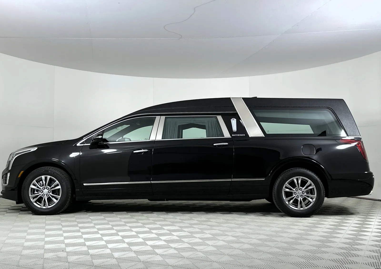 Sleek black hearse vehicle with tinted windows on a checkered floor in a white studio space