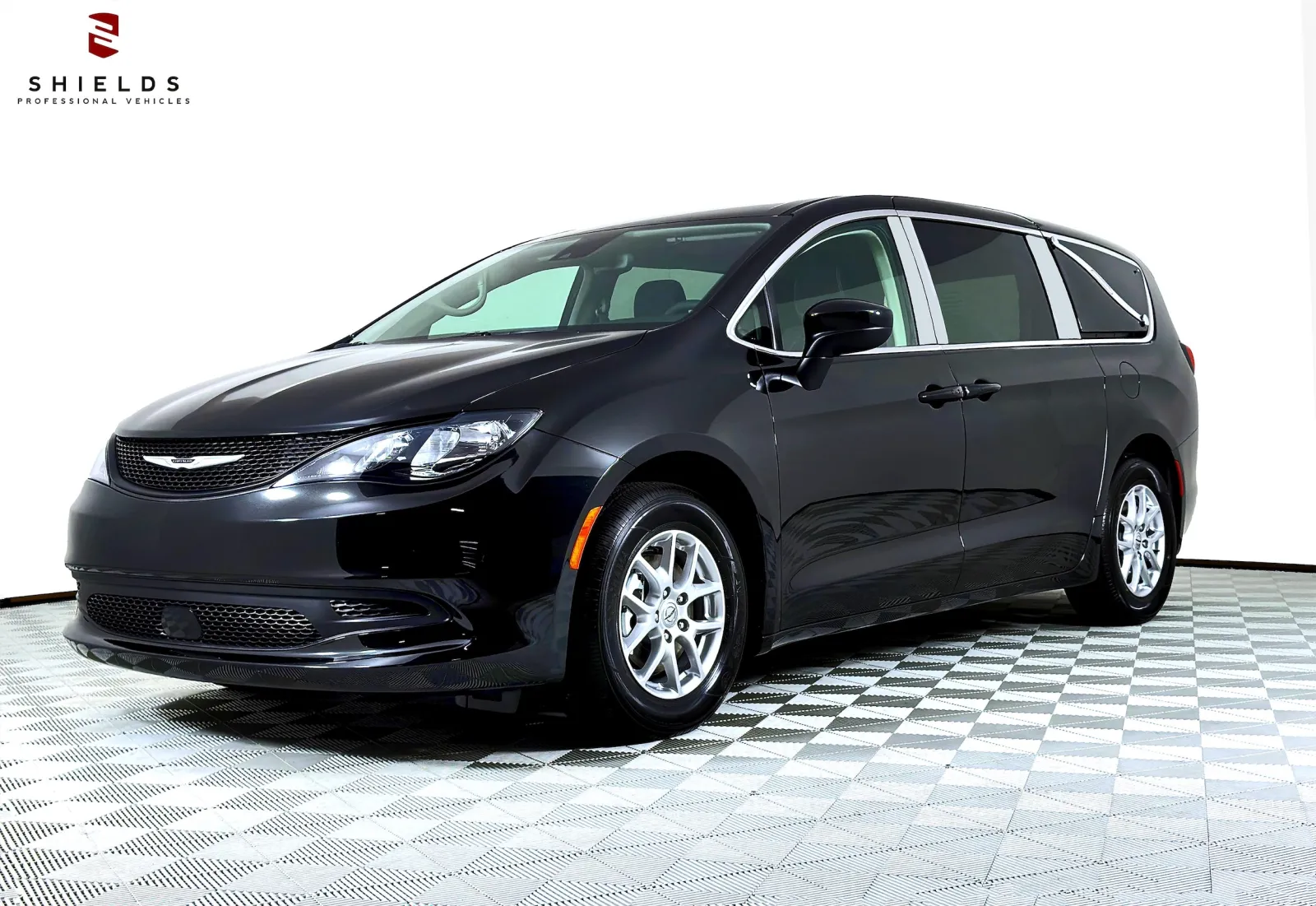 Black Chrysler minivan showcased on a checkered floor with bright lighting.