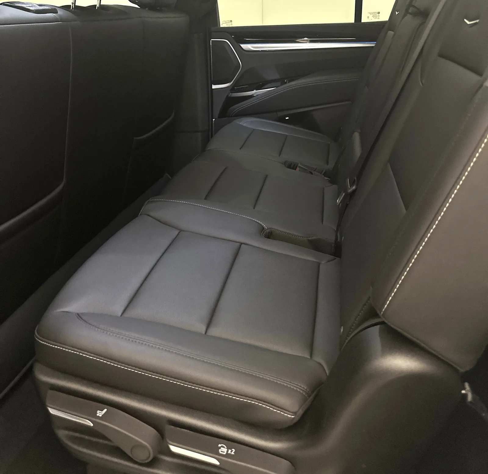 Backseat of a luxury vehicle featuring black leather upholstery with white stitching and adjustable controls.