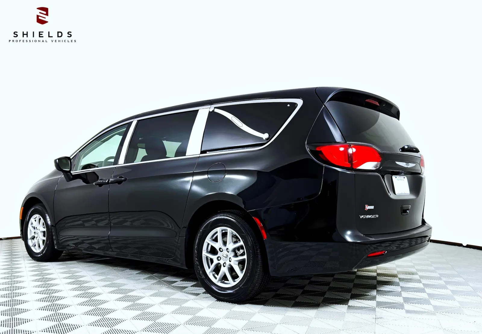 Black Chrysler Pacifica minivan parked on a checkered floor with natural lighting.