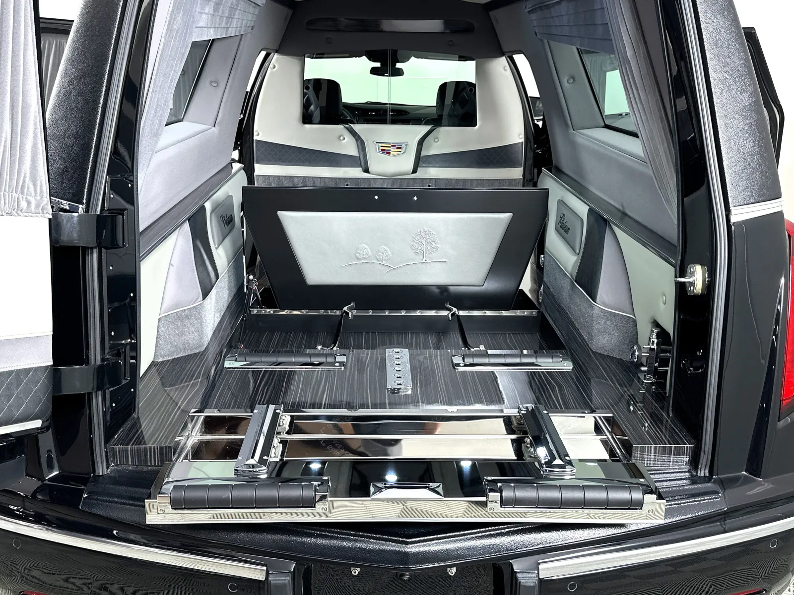 Interior of a luxury hearse with polished wood, leather details, and Cadillac emblem at the front.