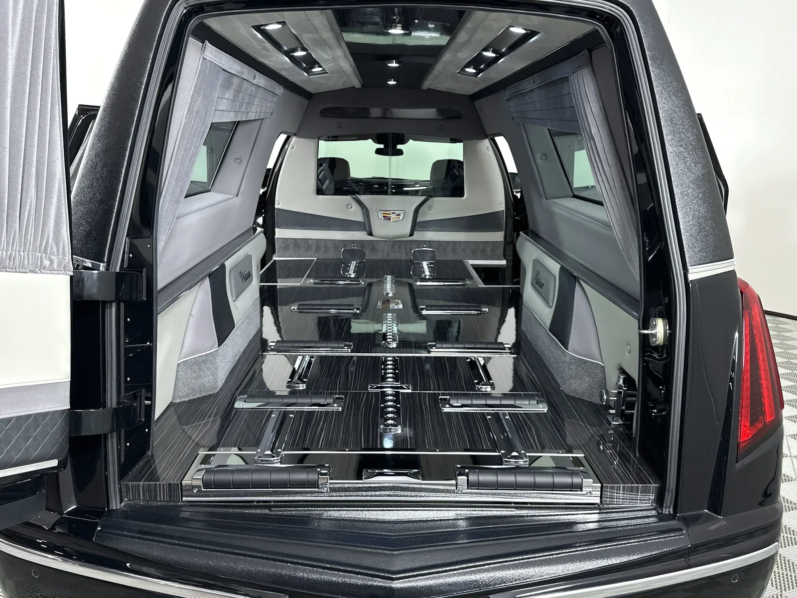 Interior view of a luxury black Cadillac hearse with a polished casket platform and elegant gray upholstery.