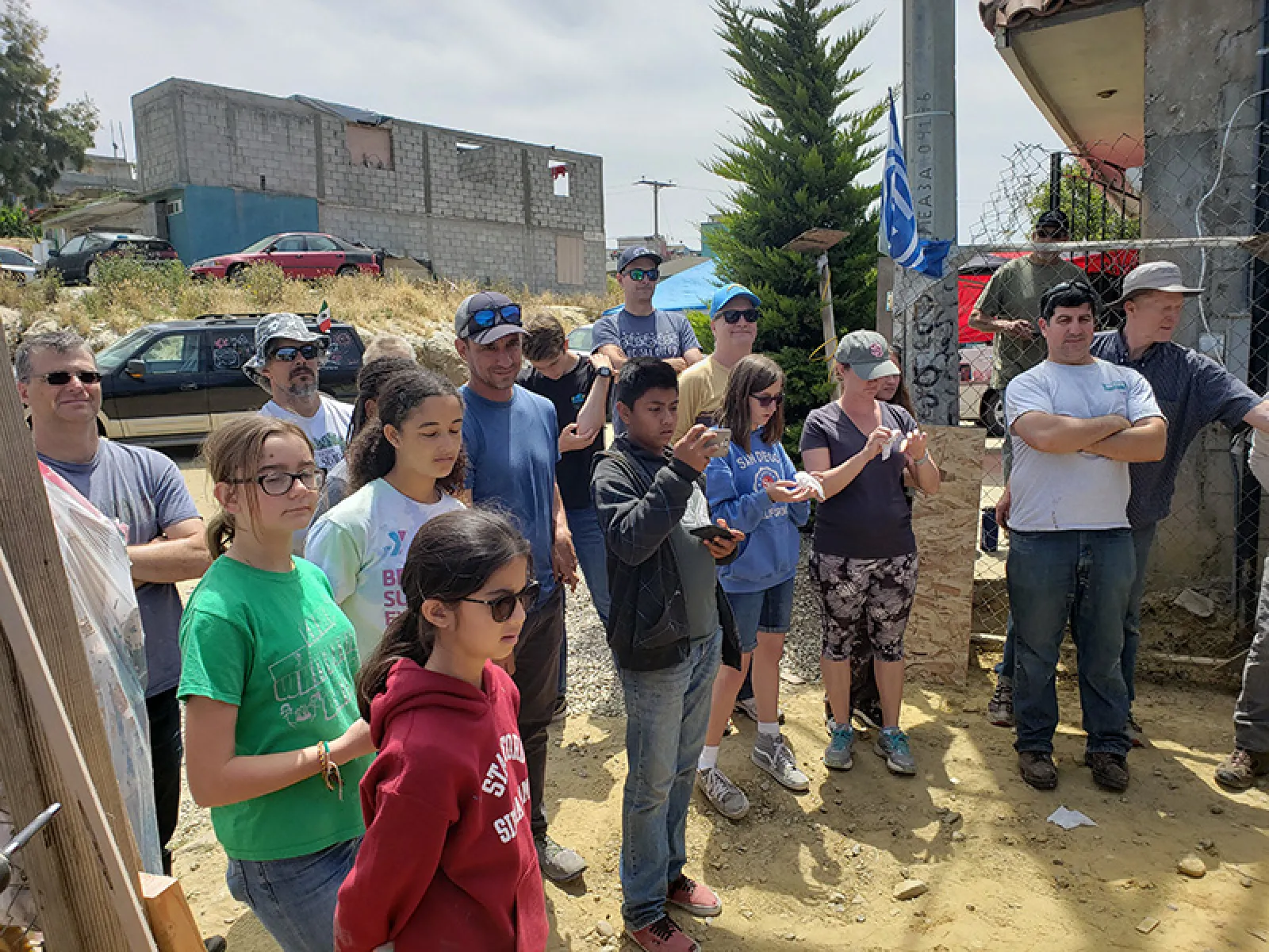 Group of people of various ages gathered outdoors near a construction site on sunny day