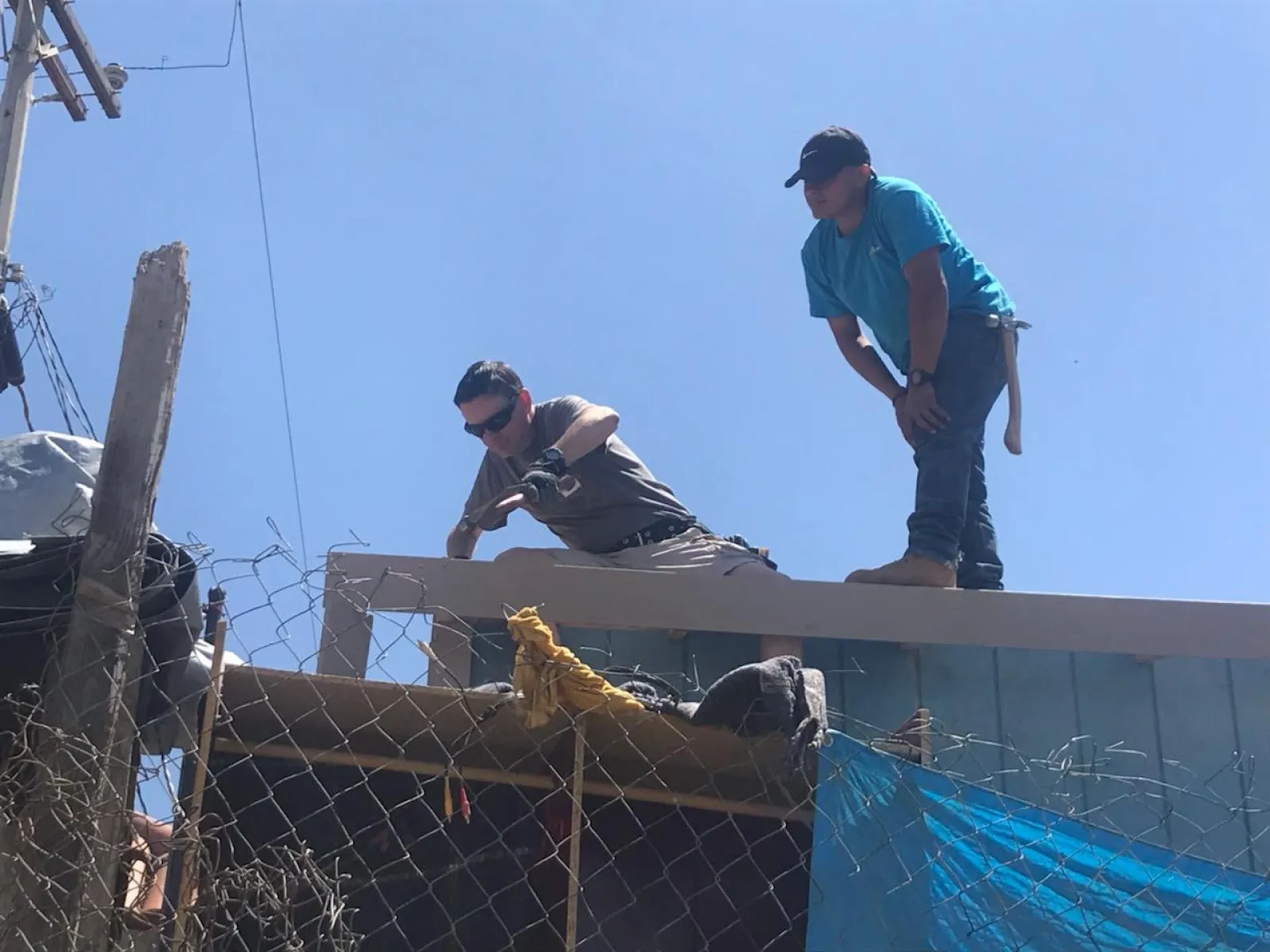 Two construction workers on a rooftop under clear blue sky working on building framework.