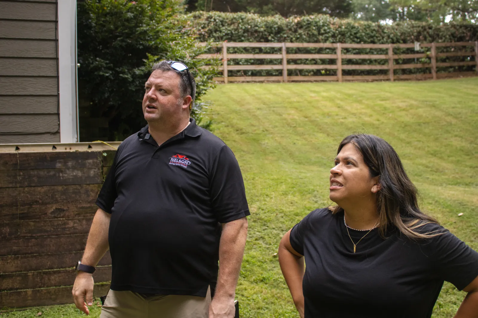Two Nelson Exteriors team members standing near a house and wooden fence, inspecting property and discussing exterior work in a grassy yard setting in Atlanta