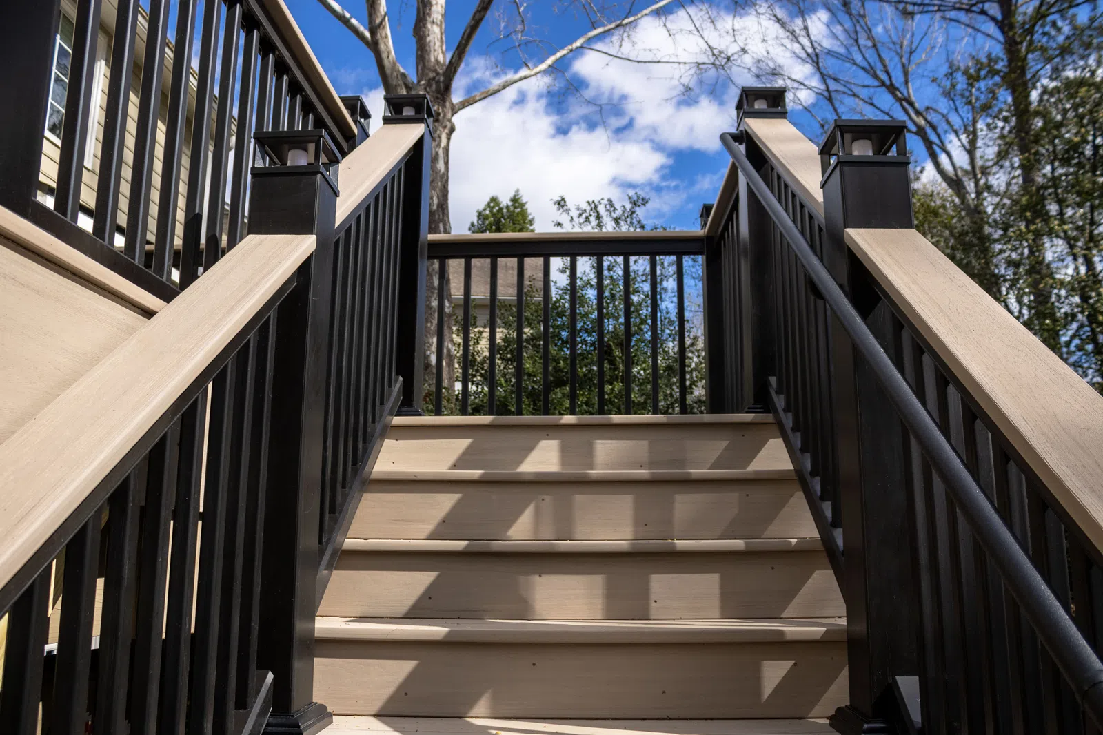 A low-angle view looking up a set of new composite deck stairs featuring modern black railings and solar post cap lights installed by expert Marietta deck builders, deck construction in Marietta by Nelson Exteriors.