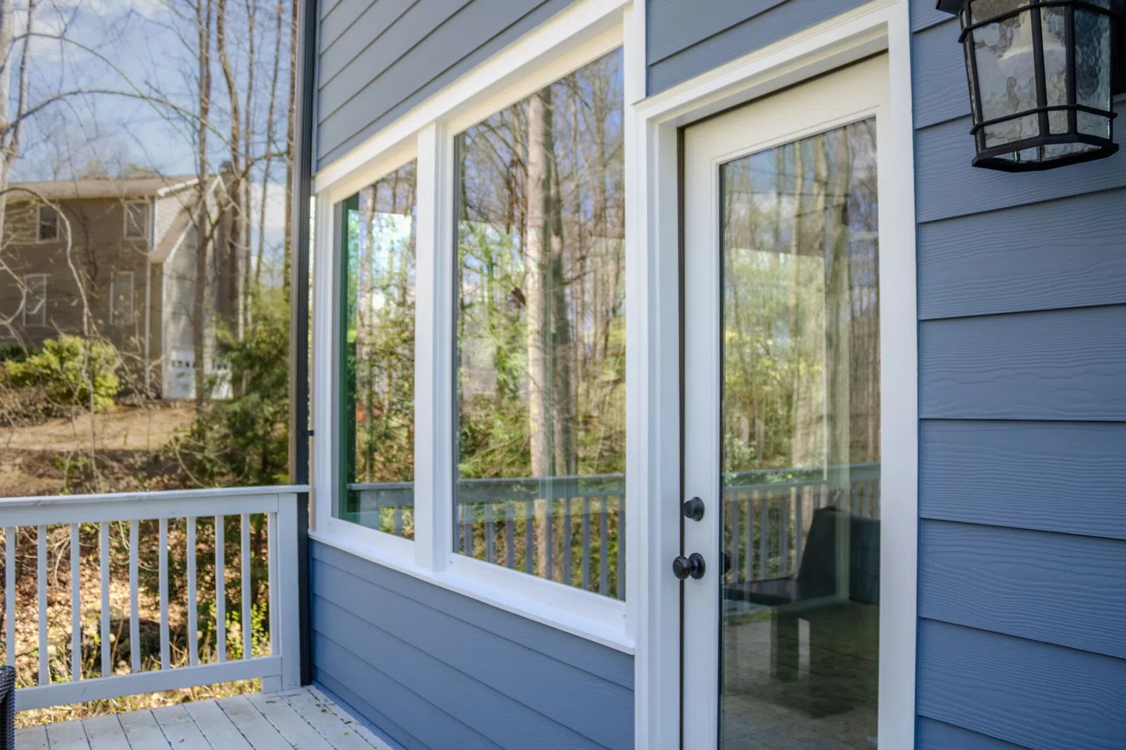 A close-up shot of newly installed blue horizontal siding, white trim windows, and a glass patio door leading to an outdoor deck, showcasing professional Marietta exterior remodeling in Marietta by Nelson Exteriors.
