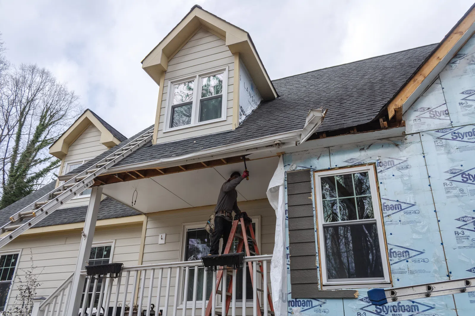 A contractor standing on a ladder on a front porch to install new soffits and repair the roof overhang during a home renovation project, providing professional Marietta exterior remodeling in Marietta by Nelson Exteriors.