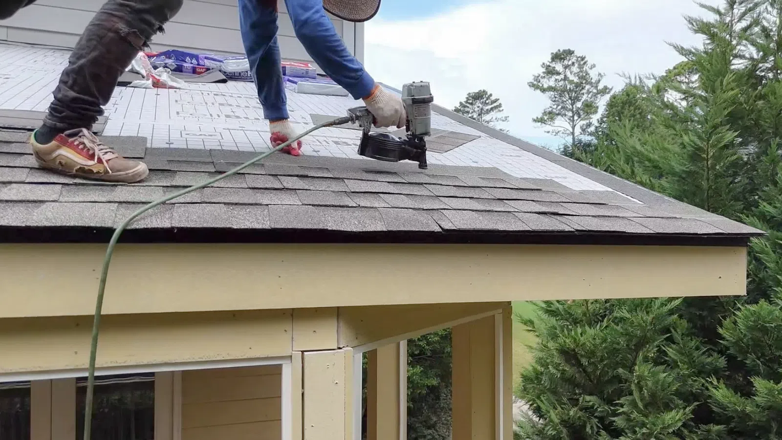 A roofer using a nail gun to install shingles and underlayment, supporting workmanship vs manufacturer roof warranty in Marietta by Nelson Exteriors.