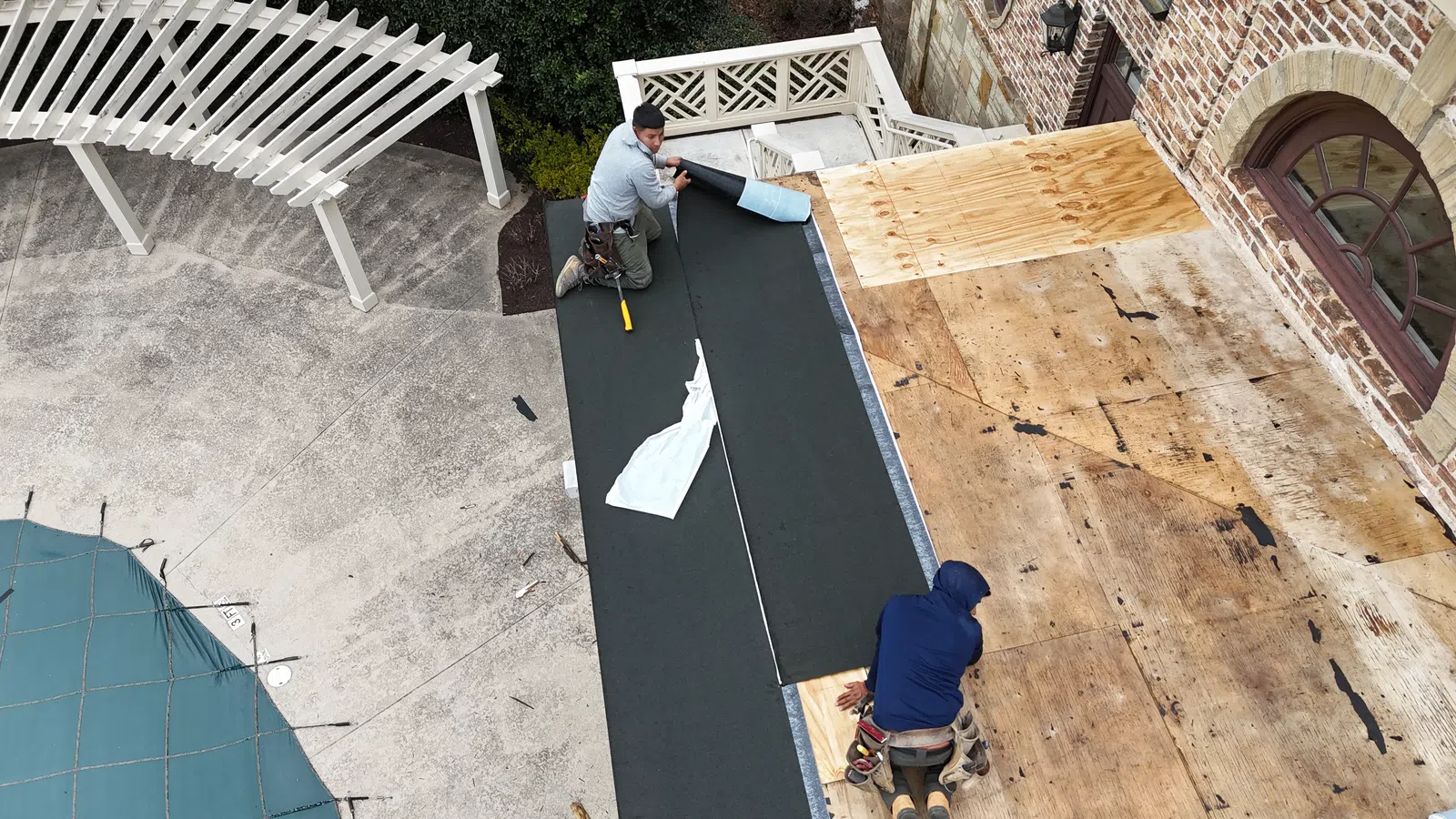 Aerial view of two contractors rolling out black modified bitumen membrane on a flat deck section, highlighting modern roof types in Georgia for flat roof installation in Marietta by Nelson Exteriors.