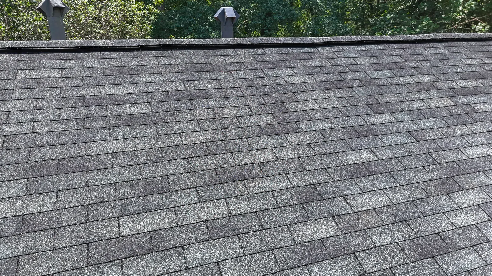 Close-up view of a dark grey three-tab asphalt shingle roof section with ridge vents, illustrating classic roof types in Georgia for residential roof inspection and repair in Marietta by Nelson Exteriors.