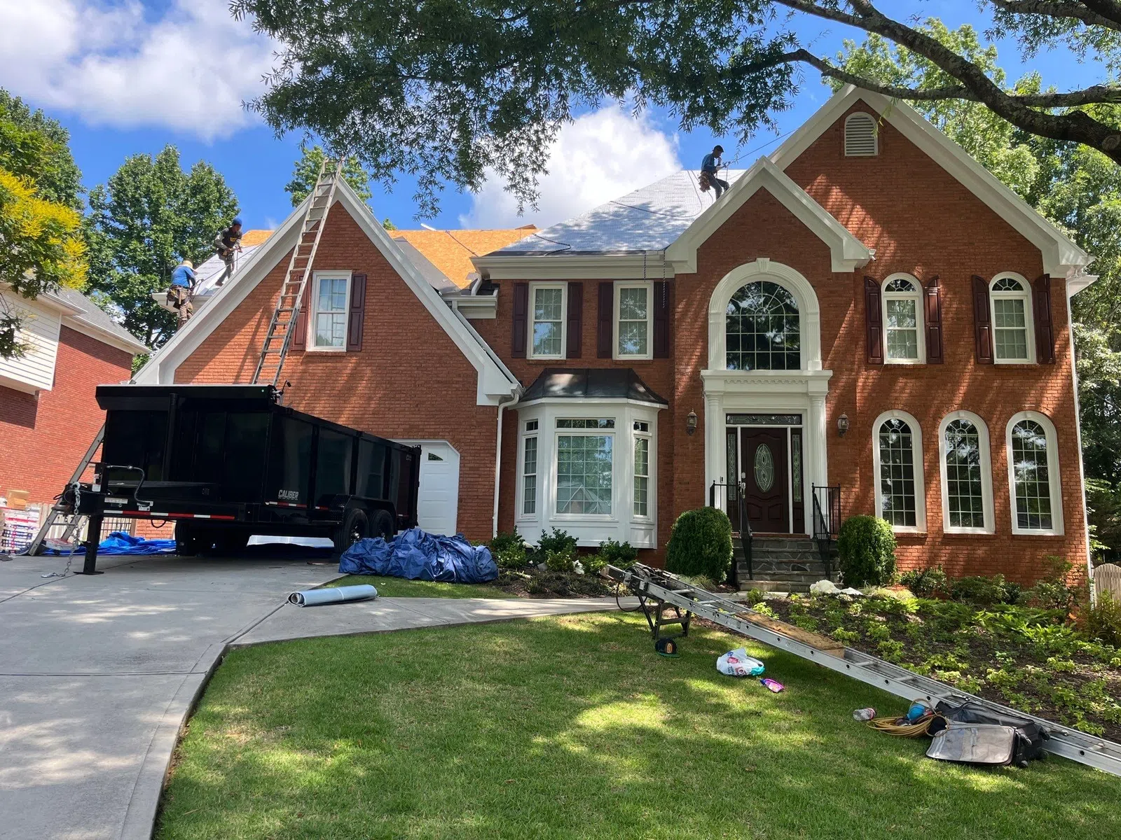 Roofing crew replacing shingles across multiple roof sections on a large two-story brick home, demonstrating how to measure what is a roofing square during roof replacement in Marietta by Nelson Exteriors.