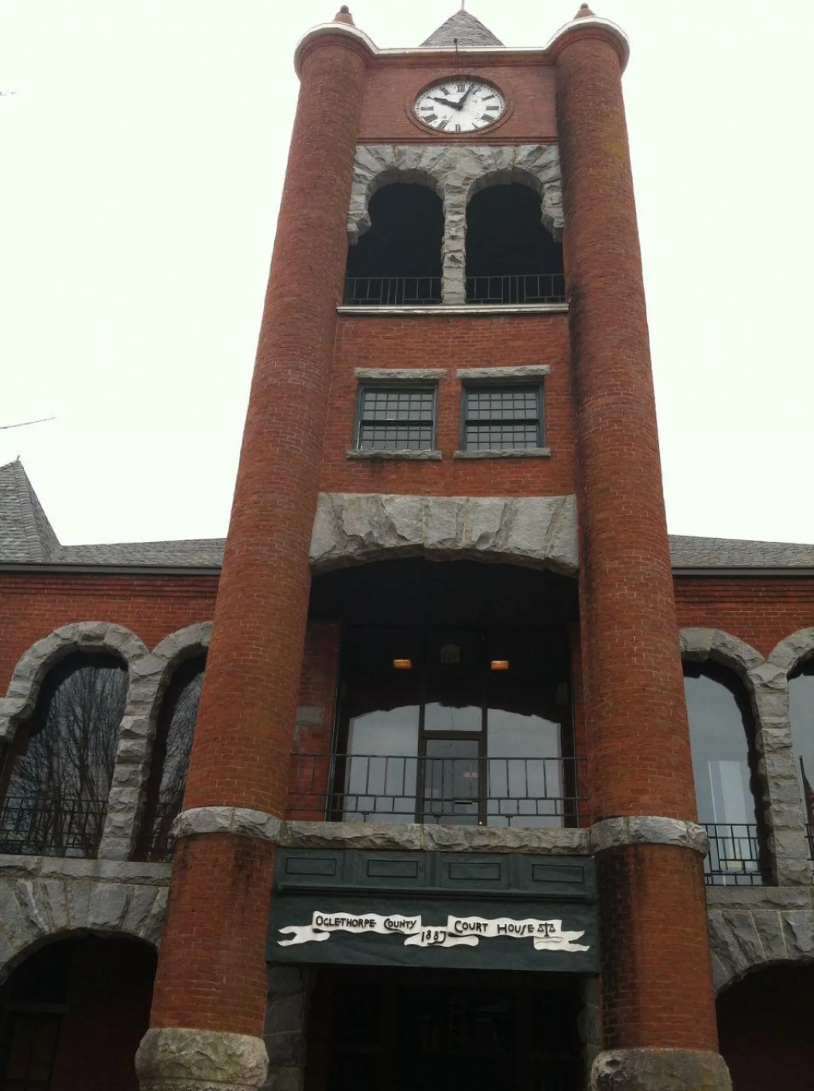 Red brick Oglethorpe County Courthouse with a clock tower and stone arch details built in 1887.