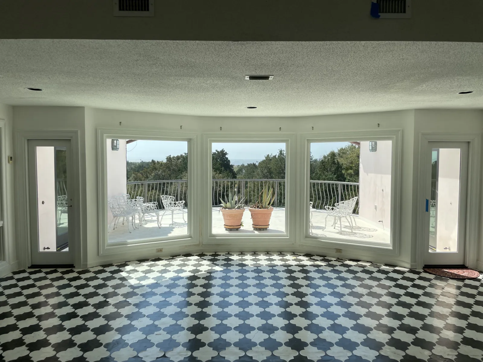 Bright room with black and white patterned floor, large windows, and a balcony with chairs and plants