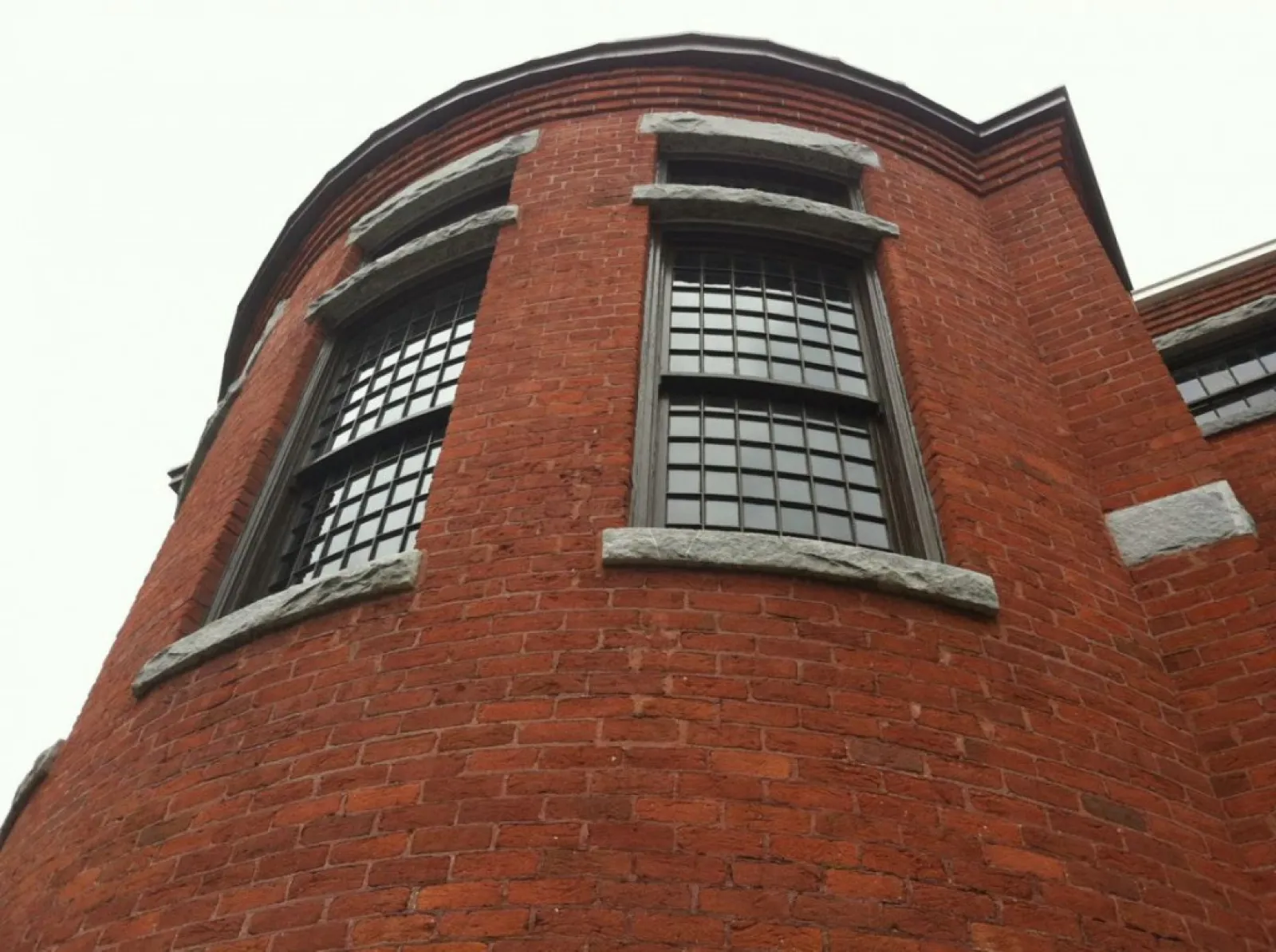 Curved red brick building facade with large multi-pane windows and stone accents under an overcast sky