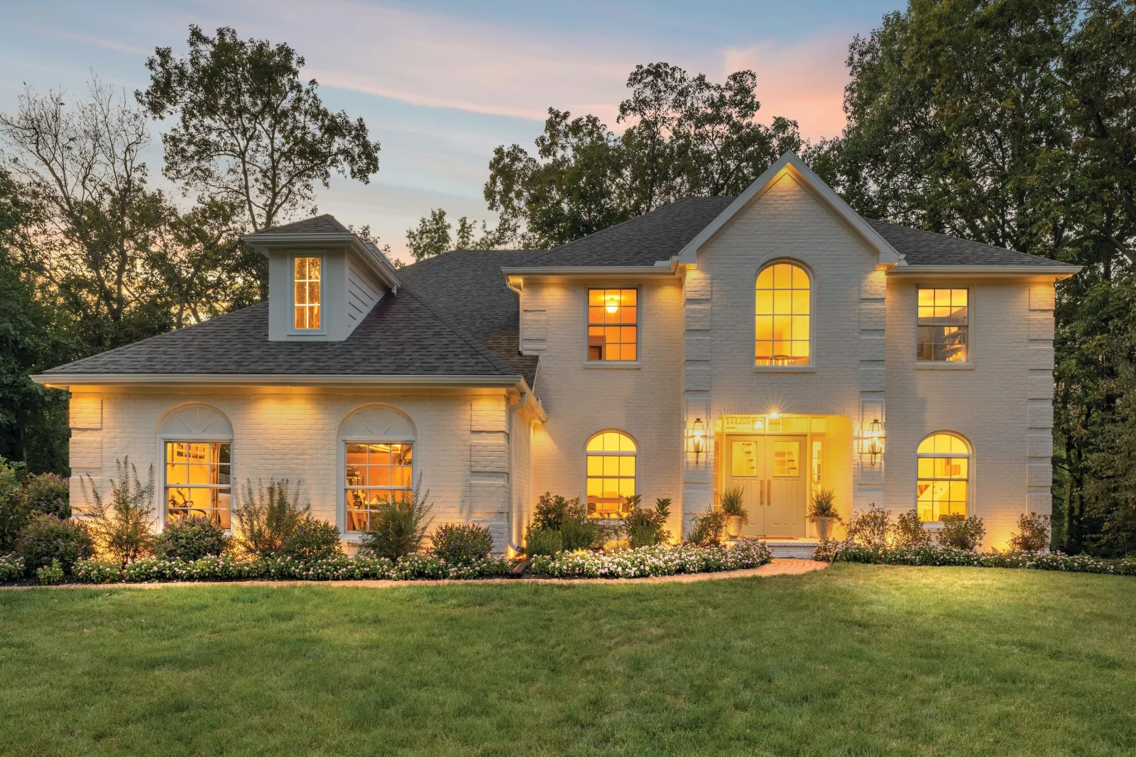 Specialty-shaped replacement windows for a luxury white brick house in Brentwood, TN, featuring warm interior lighting.