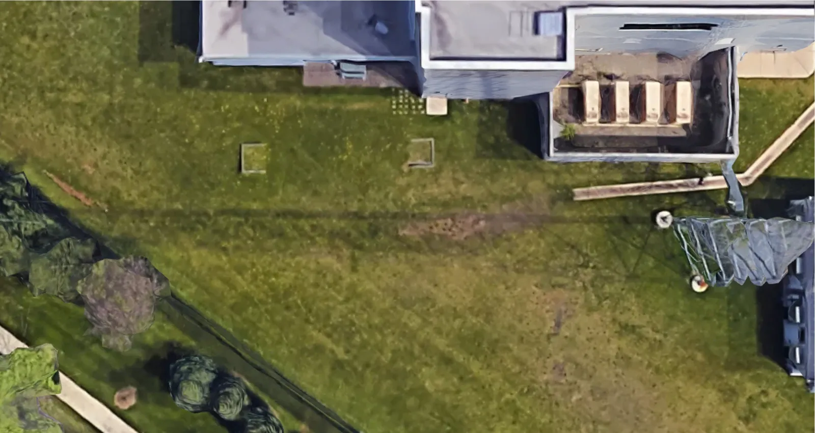 Aerial view of a building with a flat roof adjacent to a large grassy lawn and scattered trees.