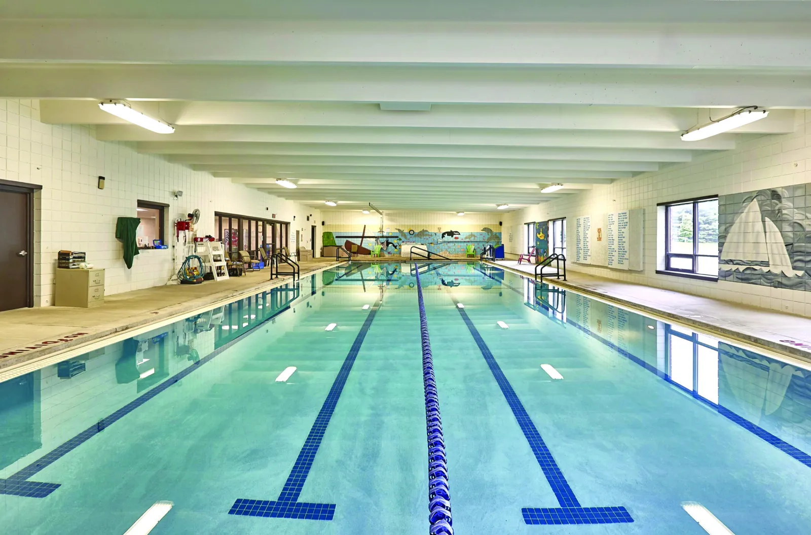 Indoor swimming pool with clear water, lanes, and mural of a beach scene on the wall.