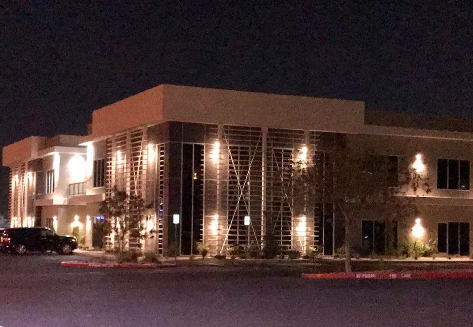 Modern two-story office building lit by exterior lights at night with parked cars nearby