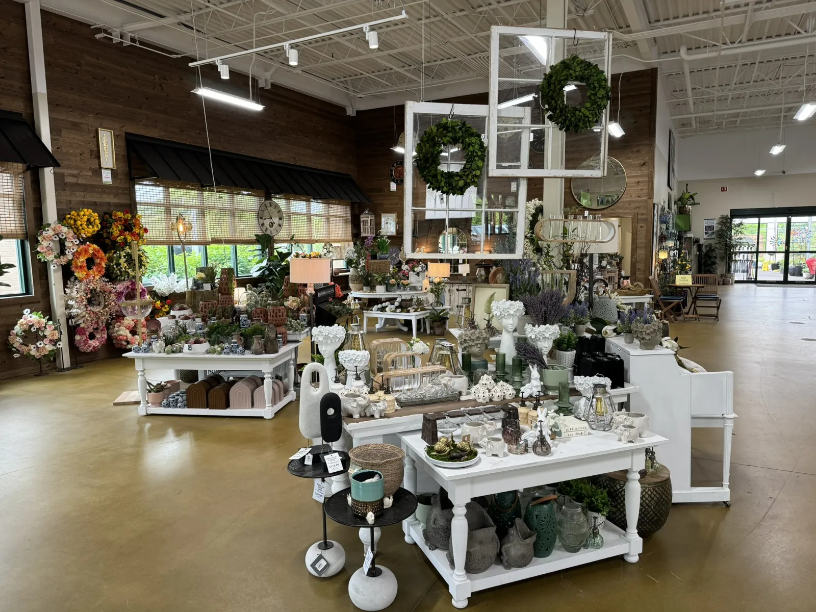 Interior of a bright home decor store displaying floral wreaths, vases, sculptures, and decorative items on tables.