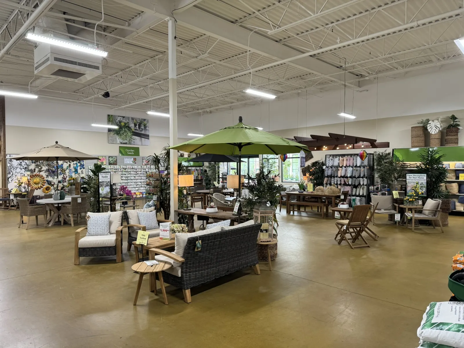 Indoor garden center showroom with outdoor furniture, umbrellas, plants, and home decor displays under bright lighting.