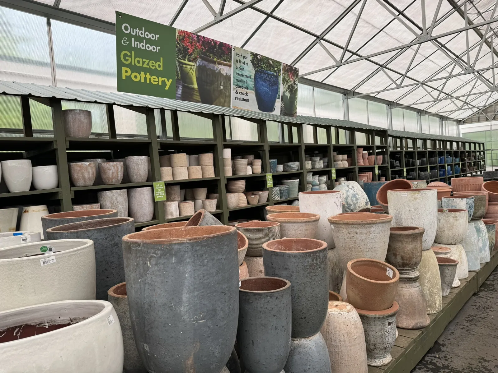 Rows of glazed pottery pots in various sizes displayed on shelves inside a greenhouse garden center.