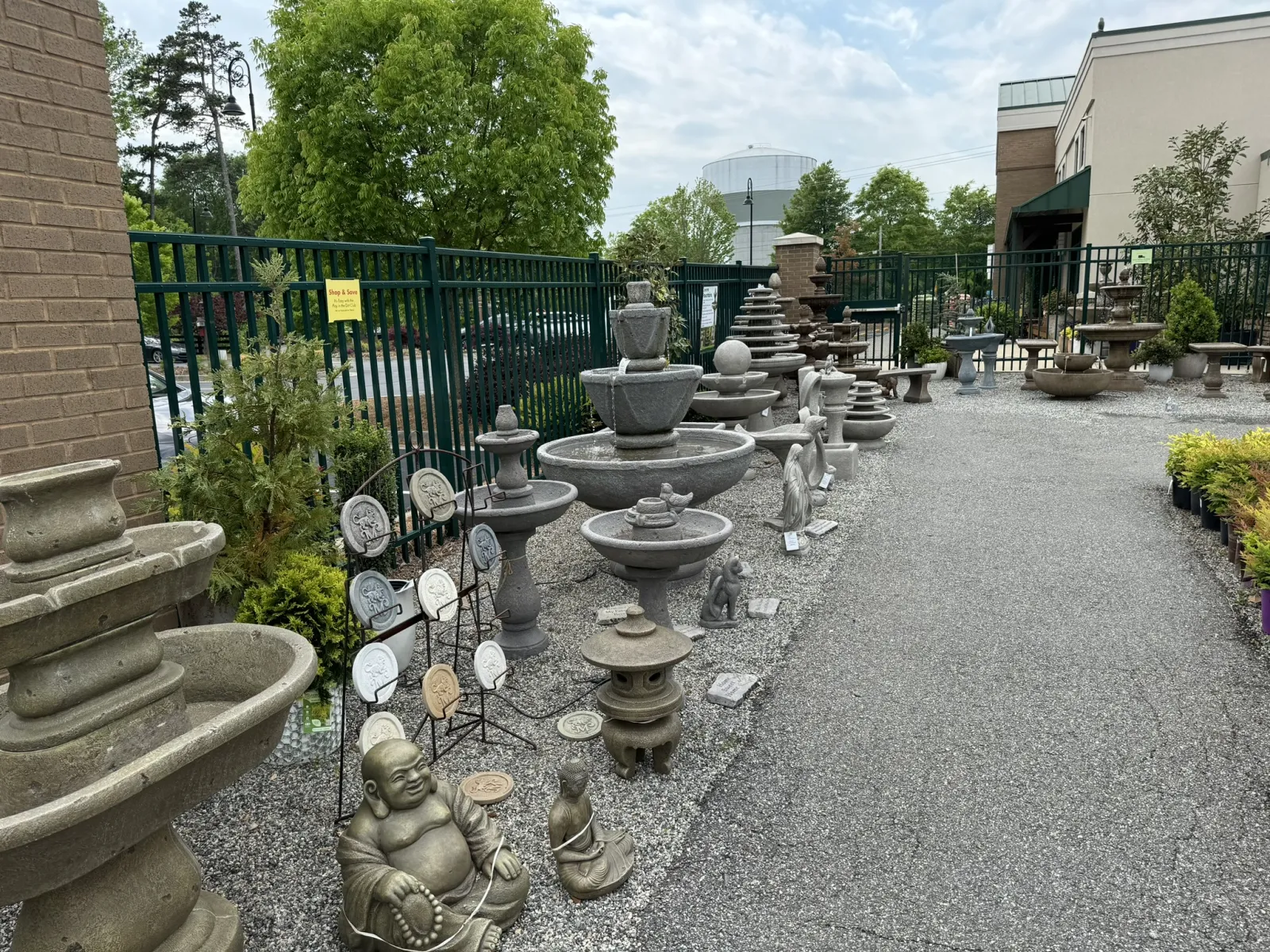 Outdoor garden center display featuring stone fountains, statues, and decorative ornaments on gravel and pavement.