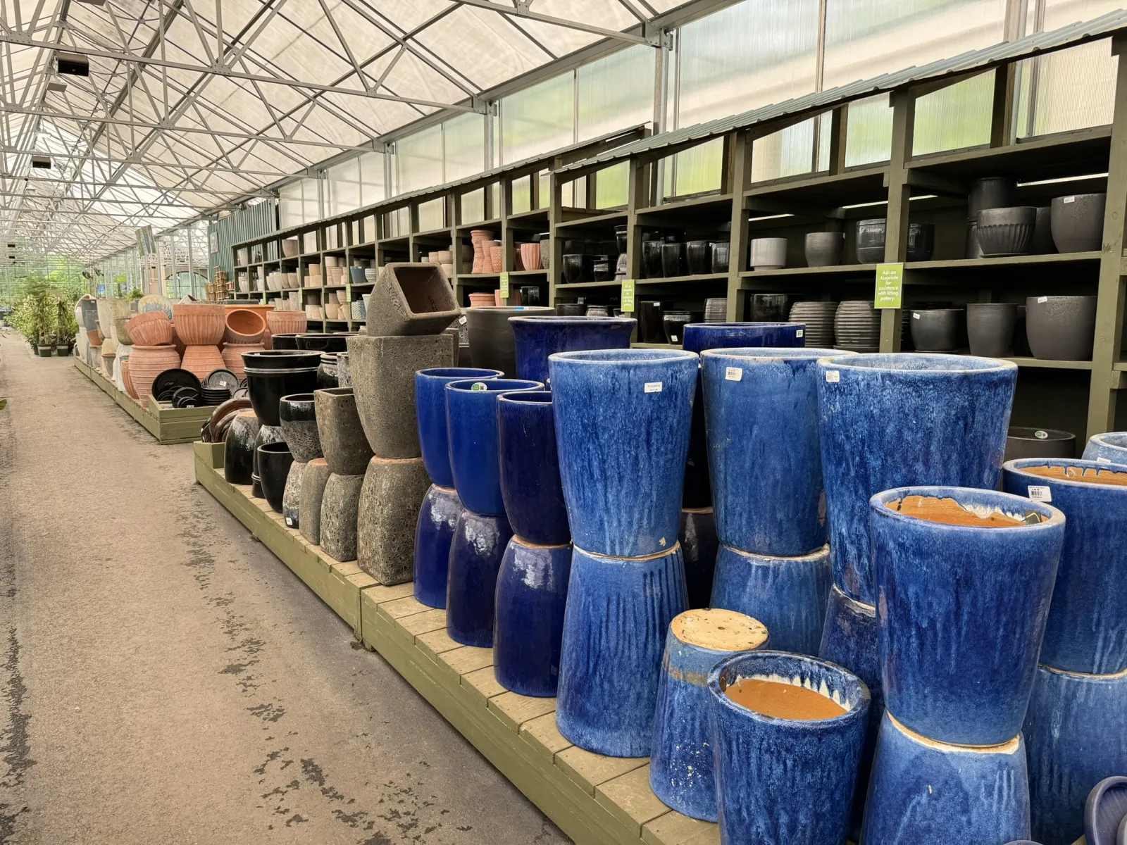 Rows of various ceramic and pottery plant pots in different shapes and colors displayed in a garden center aisle.