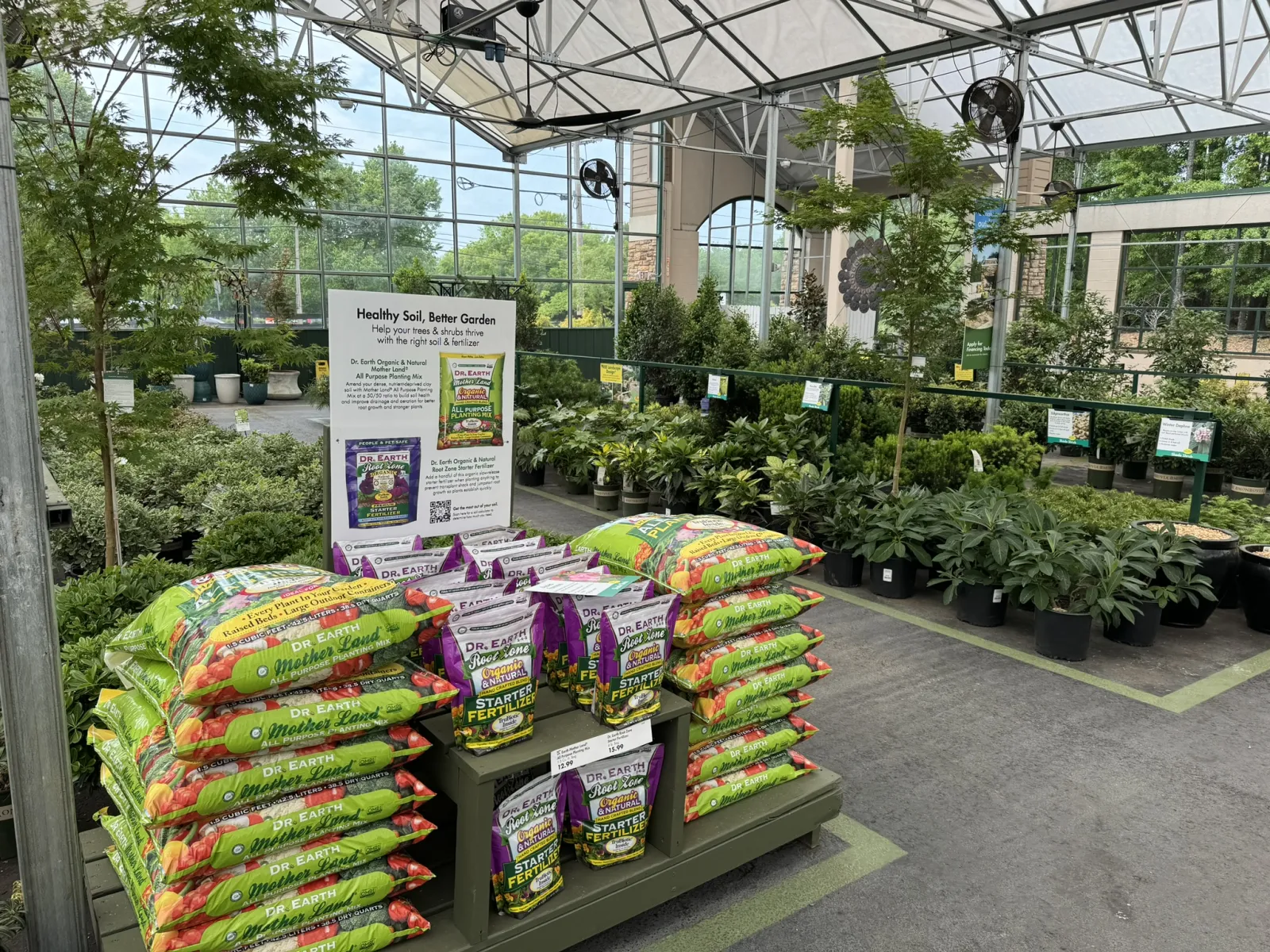 Bags of Dr. Earth soil and fertilizer displayed in a greenhouse with plants and trees in the background.