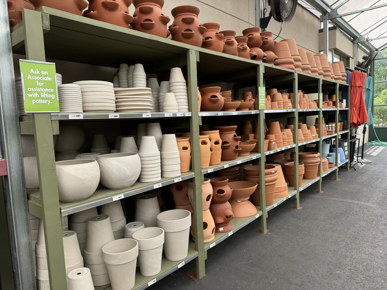 Shelves filled with various terra cotta and ceramic flower pots in a greenhouse nursery aisle.