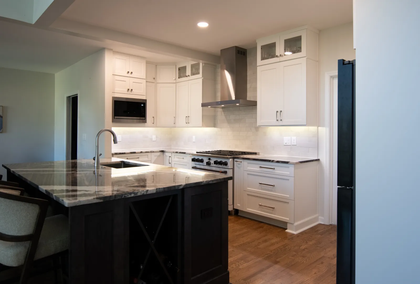 Modern kitchen with white cabinets, marble island countertop, stainless steel appliances, and hardwood floors