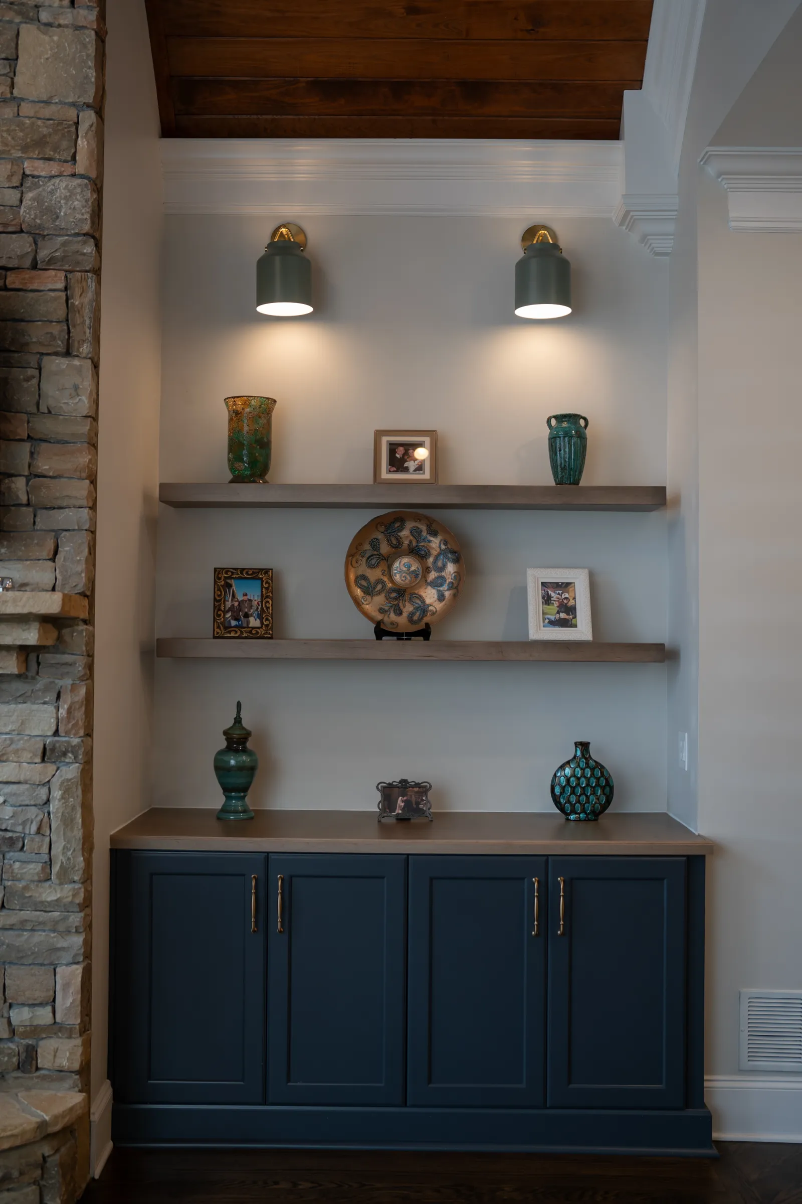 Blue cabinet with decorative vases, photo frames, and illuminated shelves in a cozy stone-walled corner.