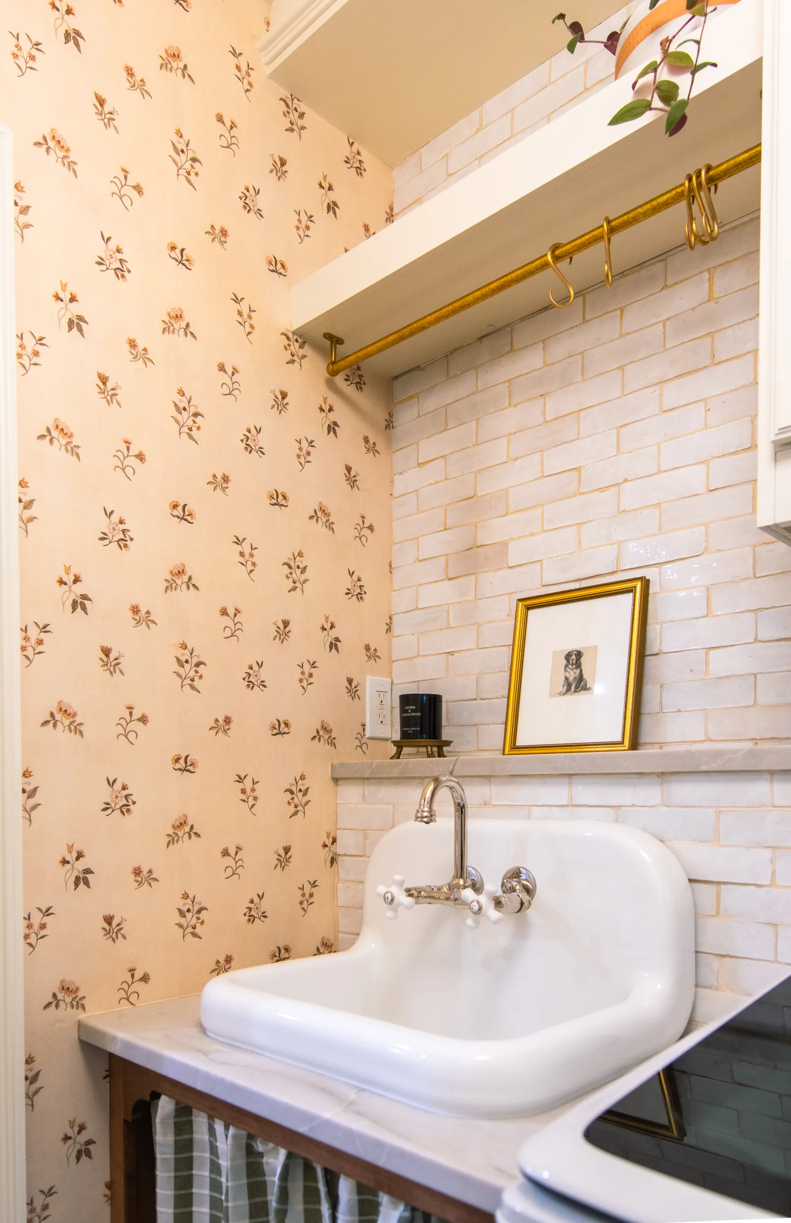 Vintage white ceramic sink with chrome faucet, floral wallpaper, and white subway tile backsplash in cozy kitchen corner.
