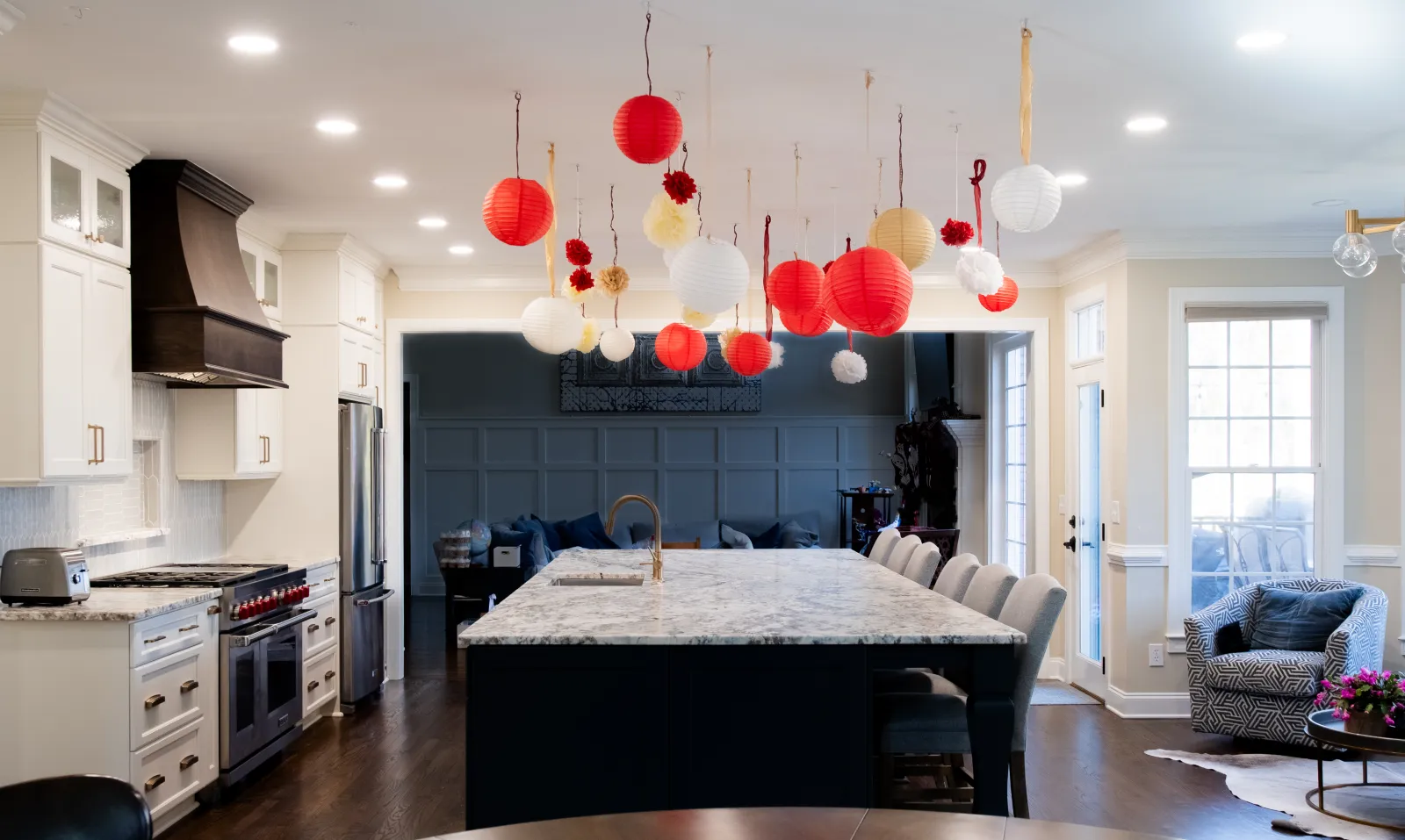 Modern kitchen with marble island, white cabinetry, stainless appliances, and red and white hanging lantern decorations.