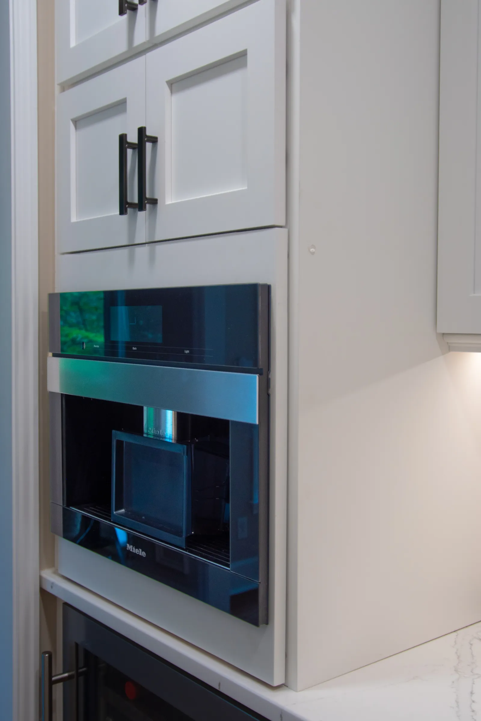 Built-in modern Miele coffee machine integrated into white kitchen cabinetry with black handles.