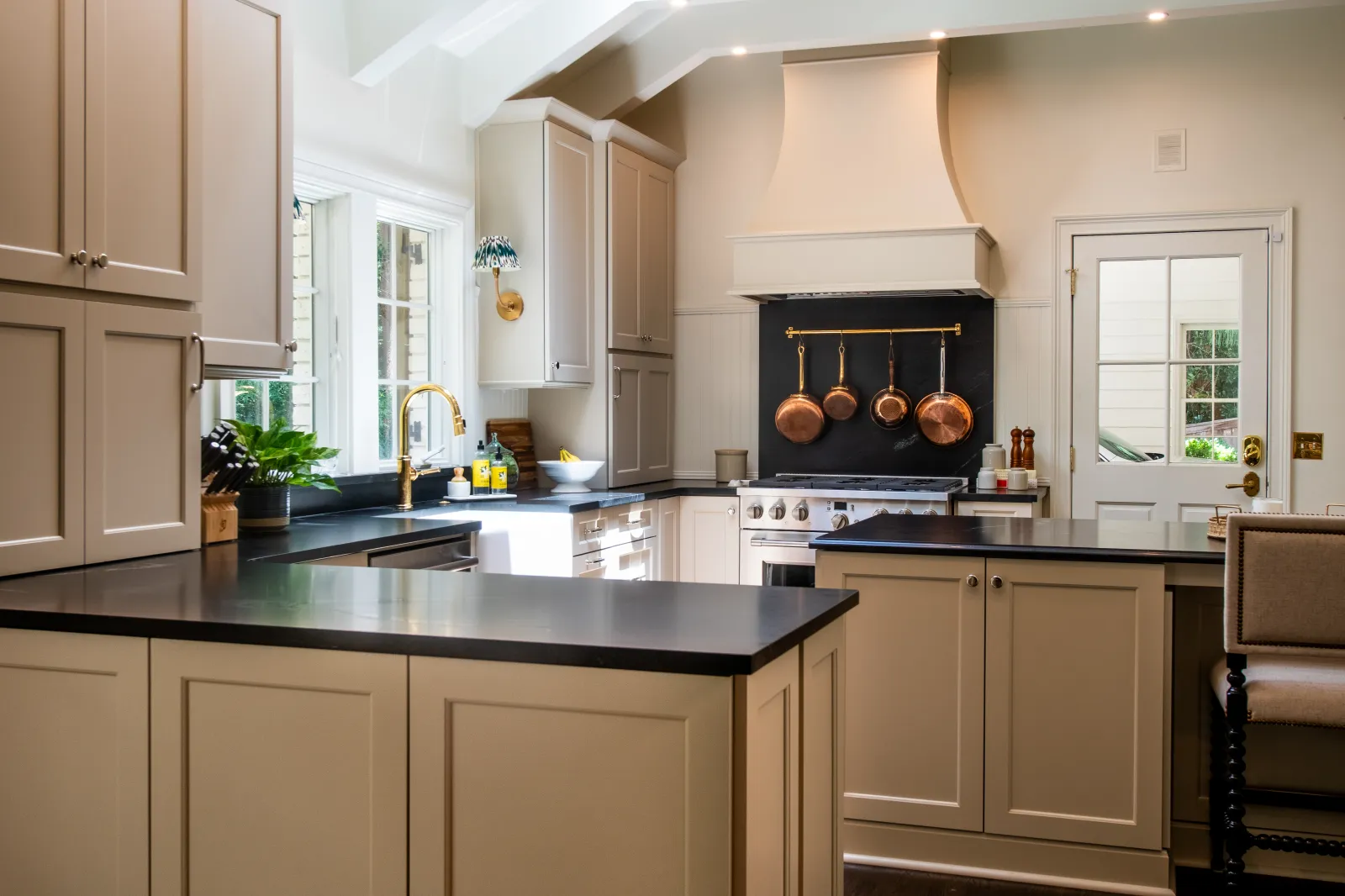 Bright modern kitchen with beige cabinets, black countertops, copper pots, and a large window for natural light