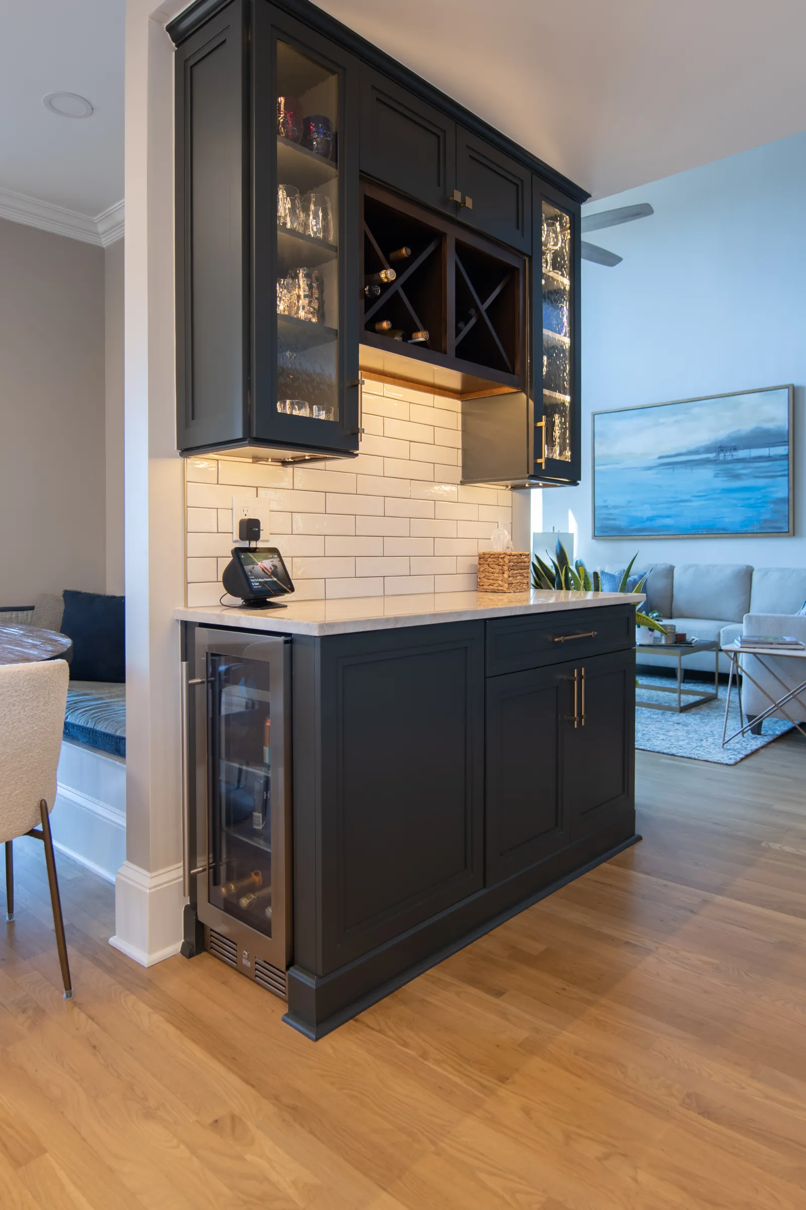 Modern kitchen bar area with black cabinets, wine fridge, glass shelves, and white subway tile backsplash.
