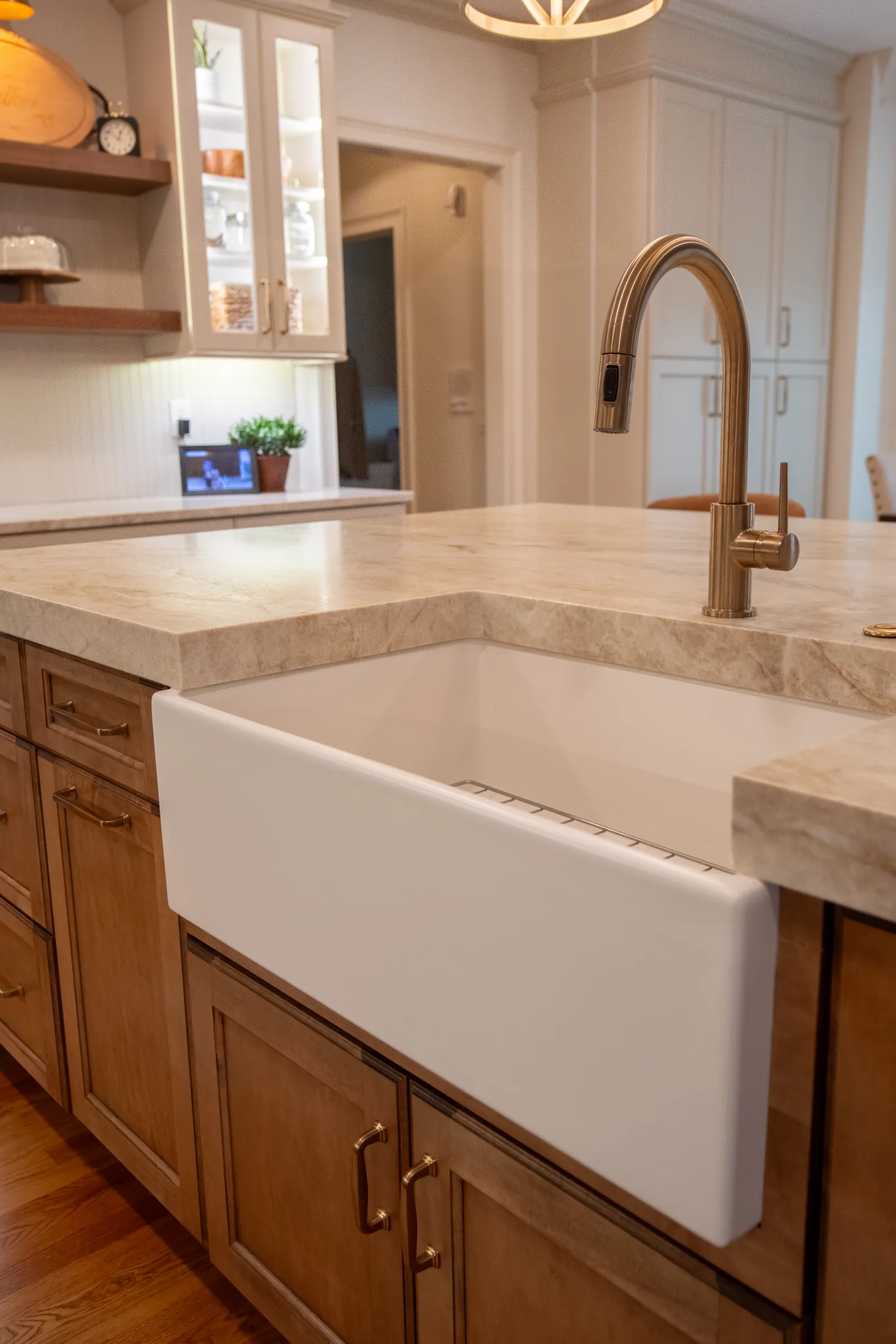 Modern kitchen with a white farmhouse sink, brass faucet, wooden cabinets, and beige marble countertop.