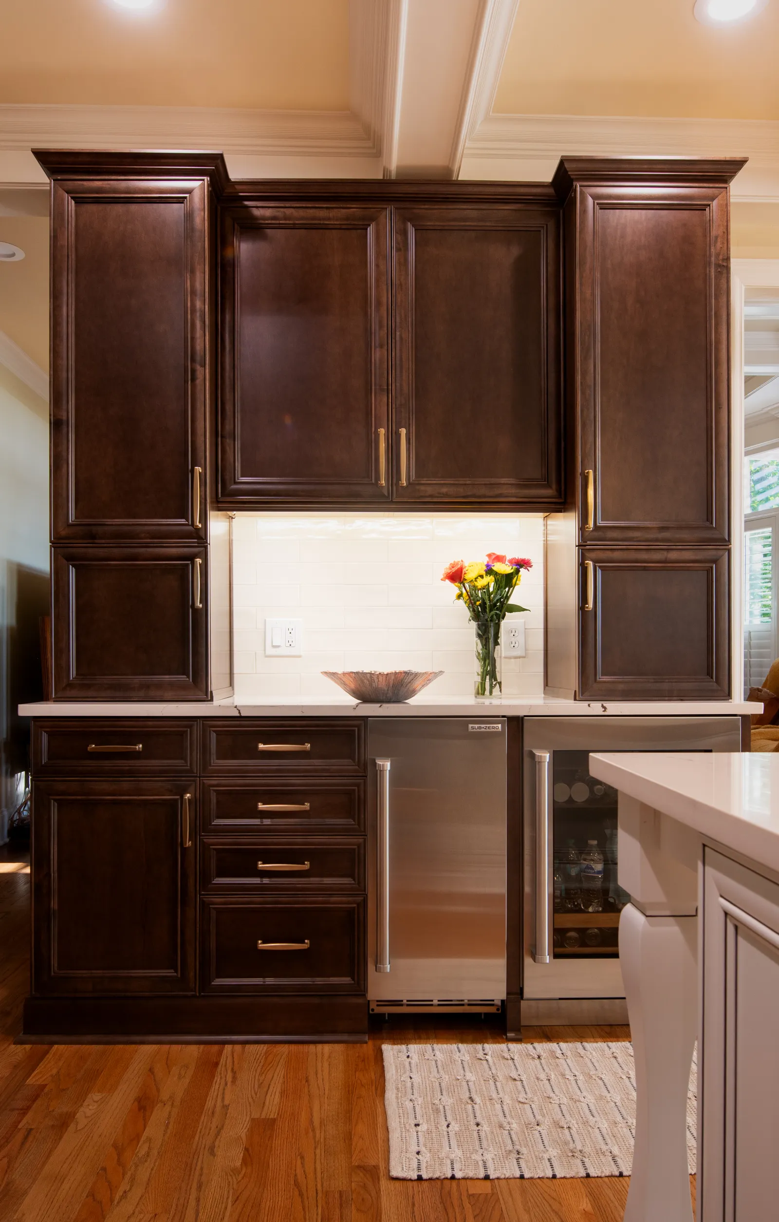 Dark wooden kitchen cabinets with stainless steel appliances, white countertop, and flowers in vase on counter.